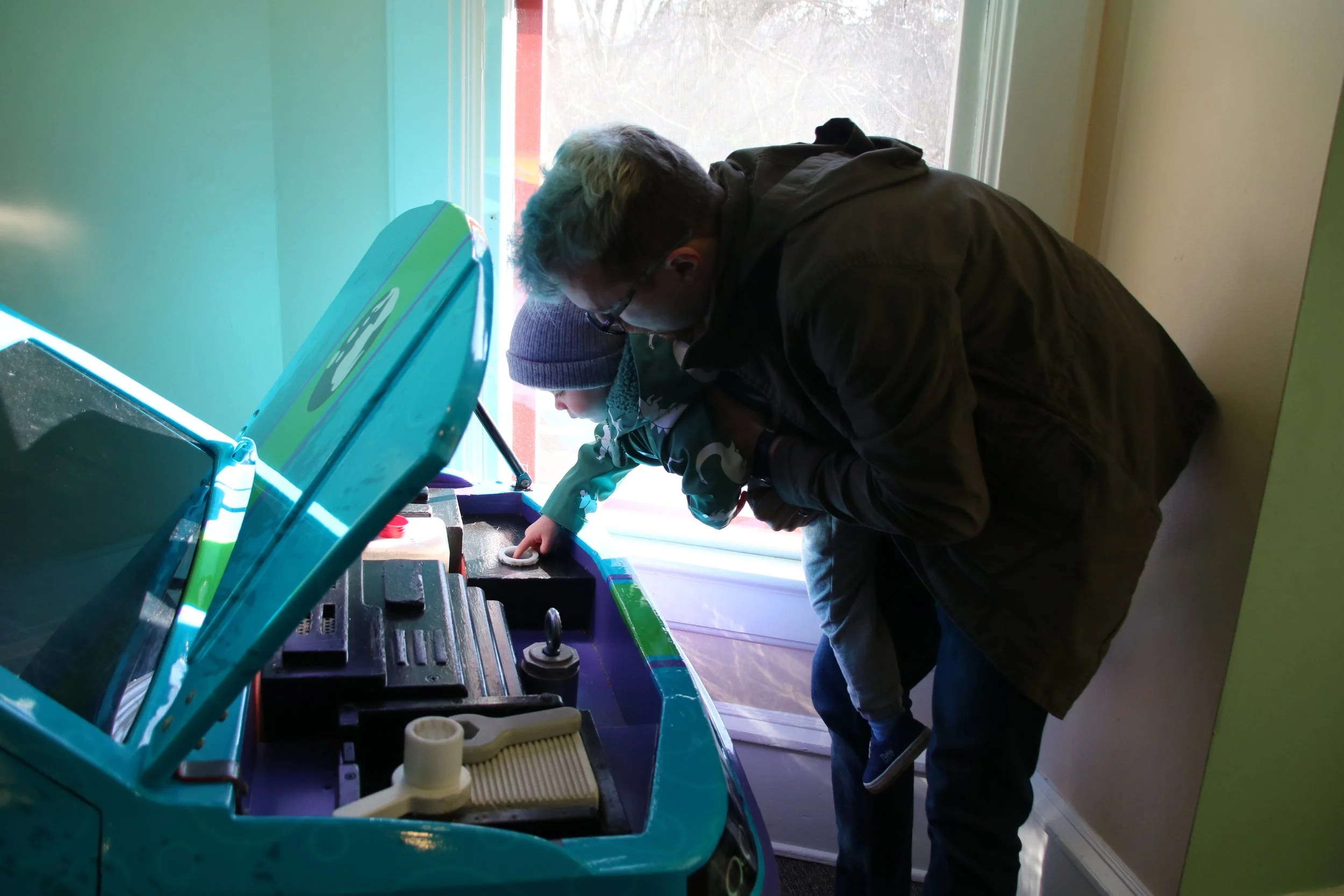 Two boys playing a vintage arcade game, one leaning over and pointing at the screen, the other standing behind them, both focused on the game.