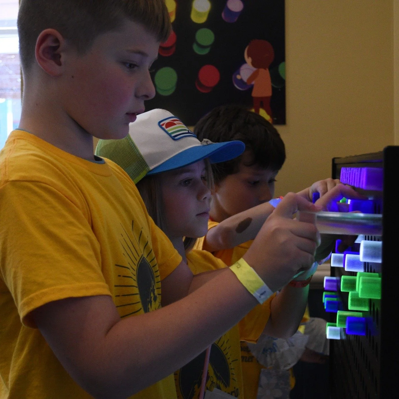 Three children playing with a colorful light board in an indoor setting.
