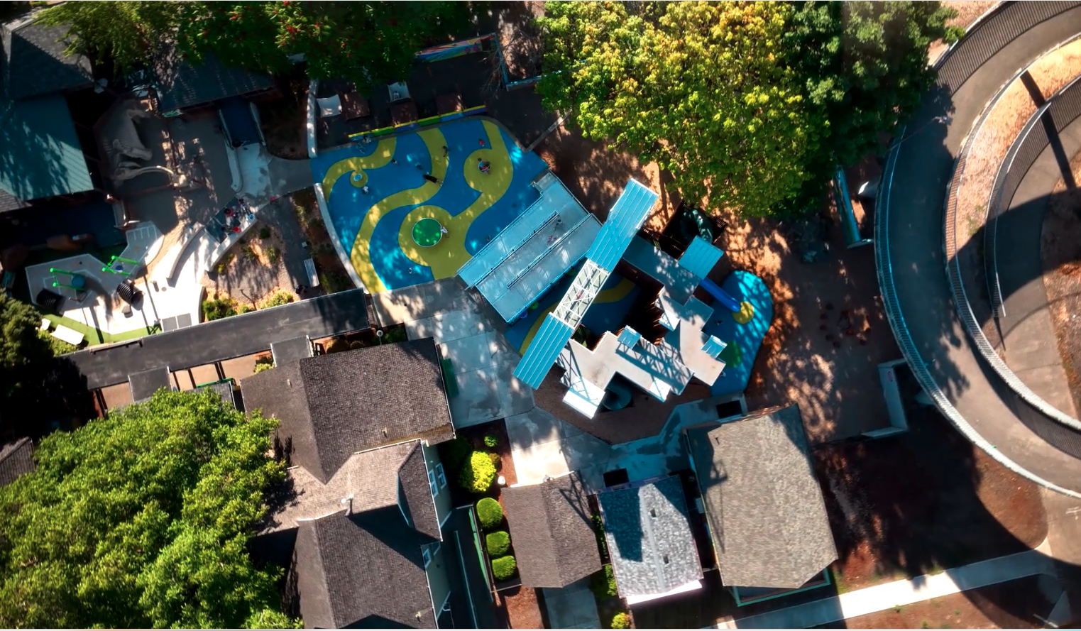 Aerial view of the Gilbert House Children's Museum campus in Salem, Oregon, showcasing the historic Victorian houses, the massive Erector Set Maze outdoor play structure, and its location adjacent to the Willamette River and Riverfront Park.