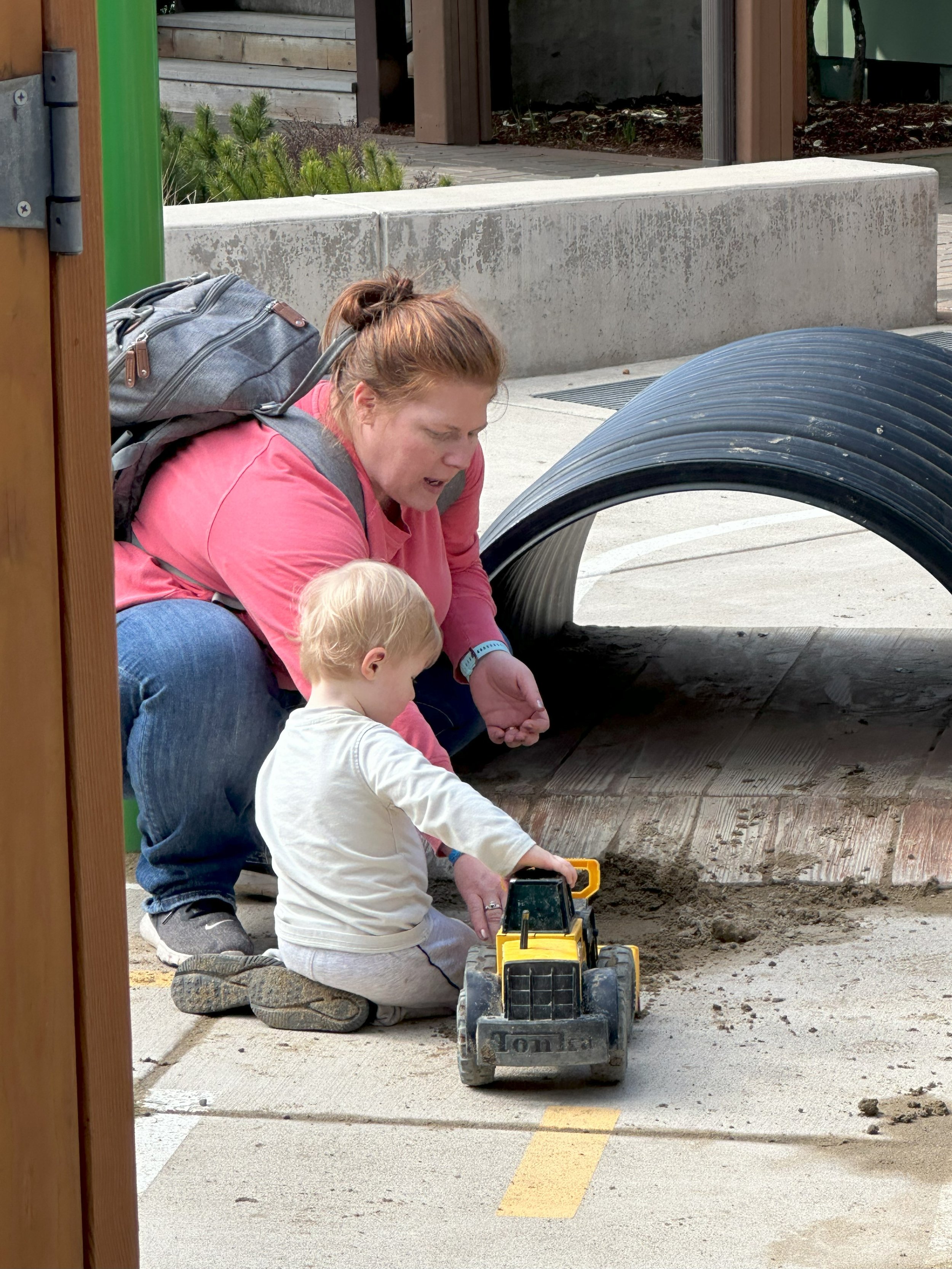 A woman and a young child playing with a toy bulldozer on a sandbox at a playground.