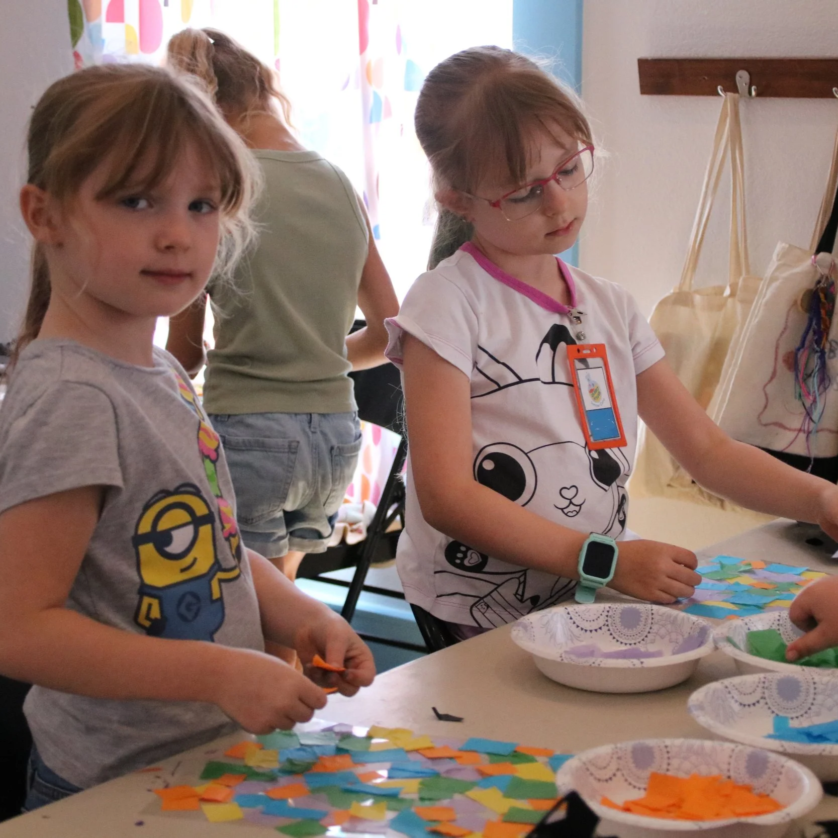 Children working on a craft project at a table with colorful paper pieces.