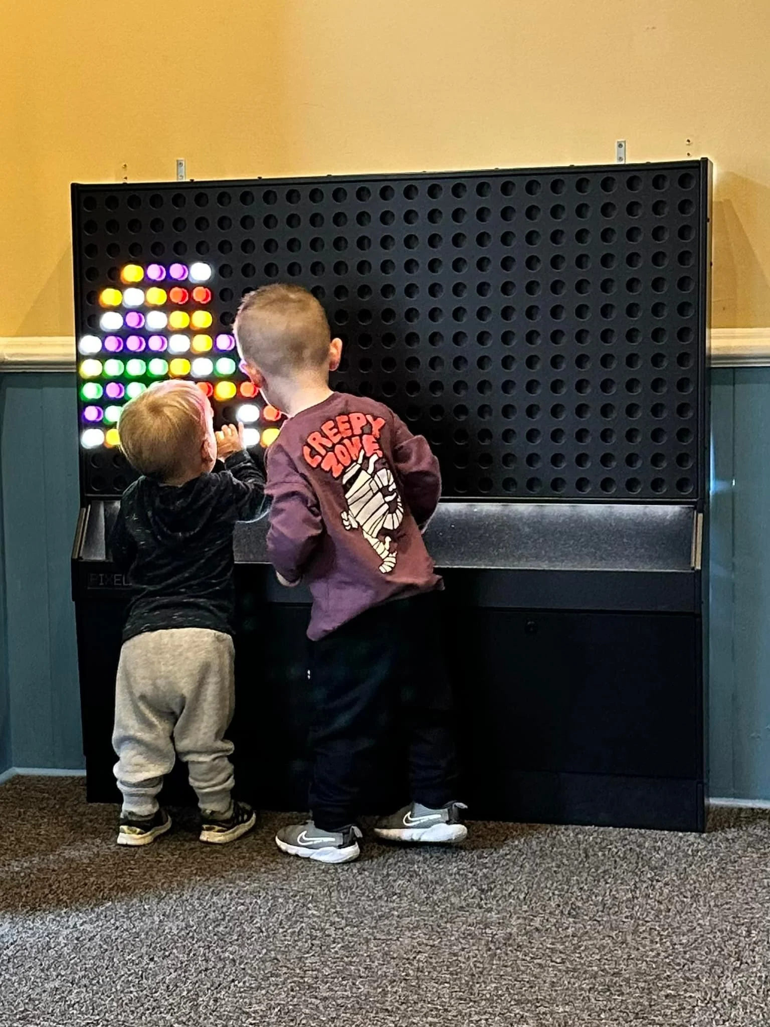 Two young boys playing a colorful pegboard game, with one boy concentrating and the other reaching for the pegs.