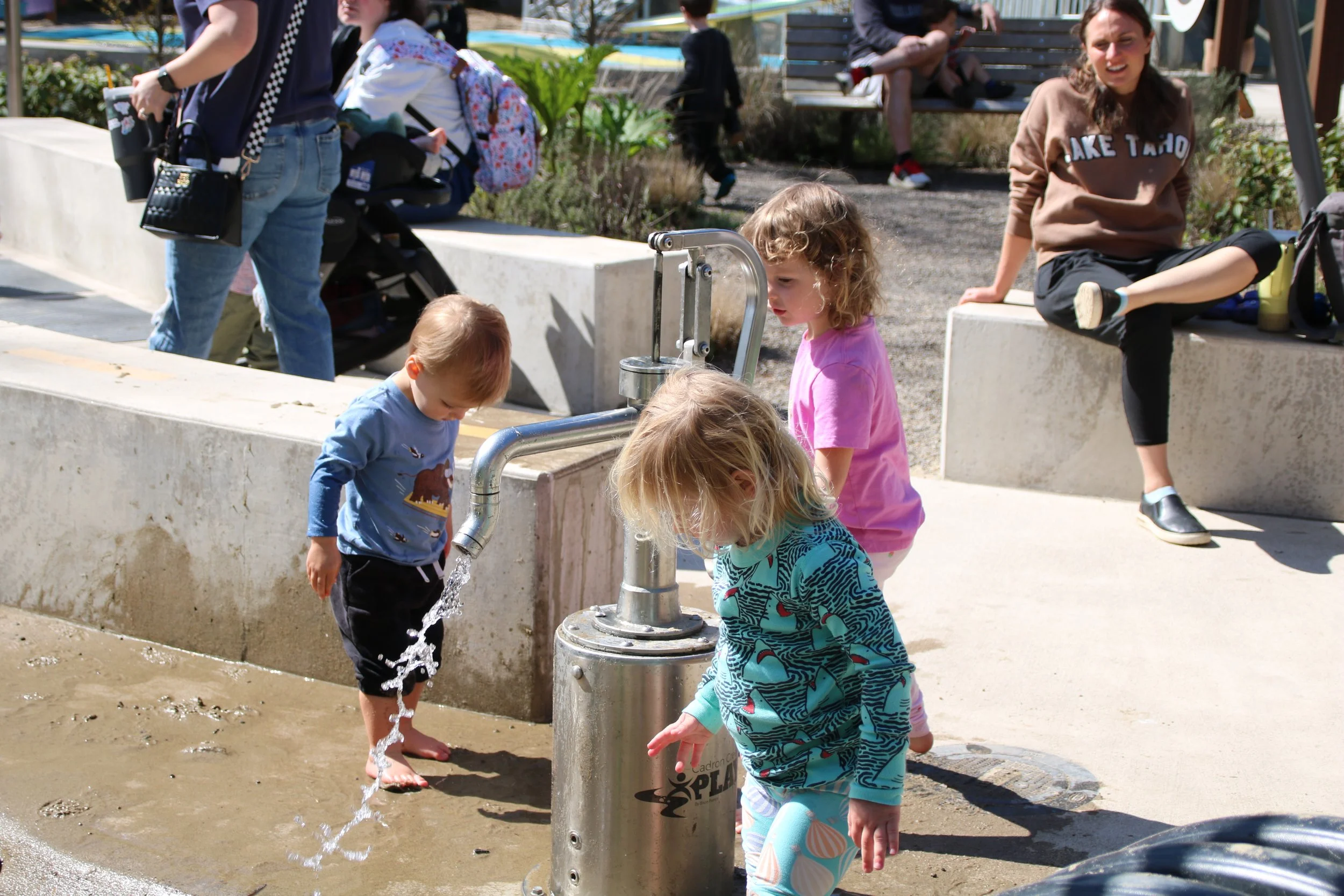 Children playing with water from an outdoor fountain in a park on a sunny day.