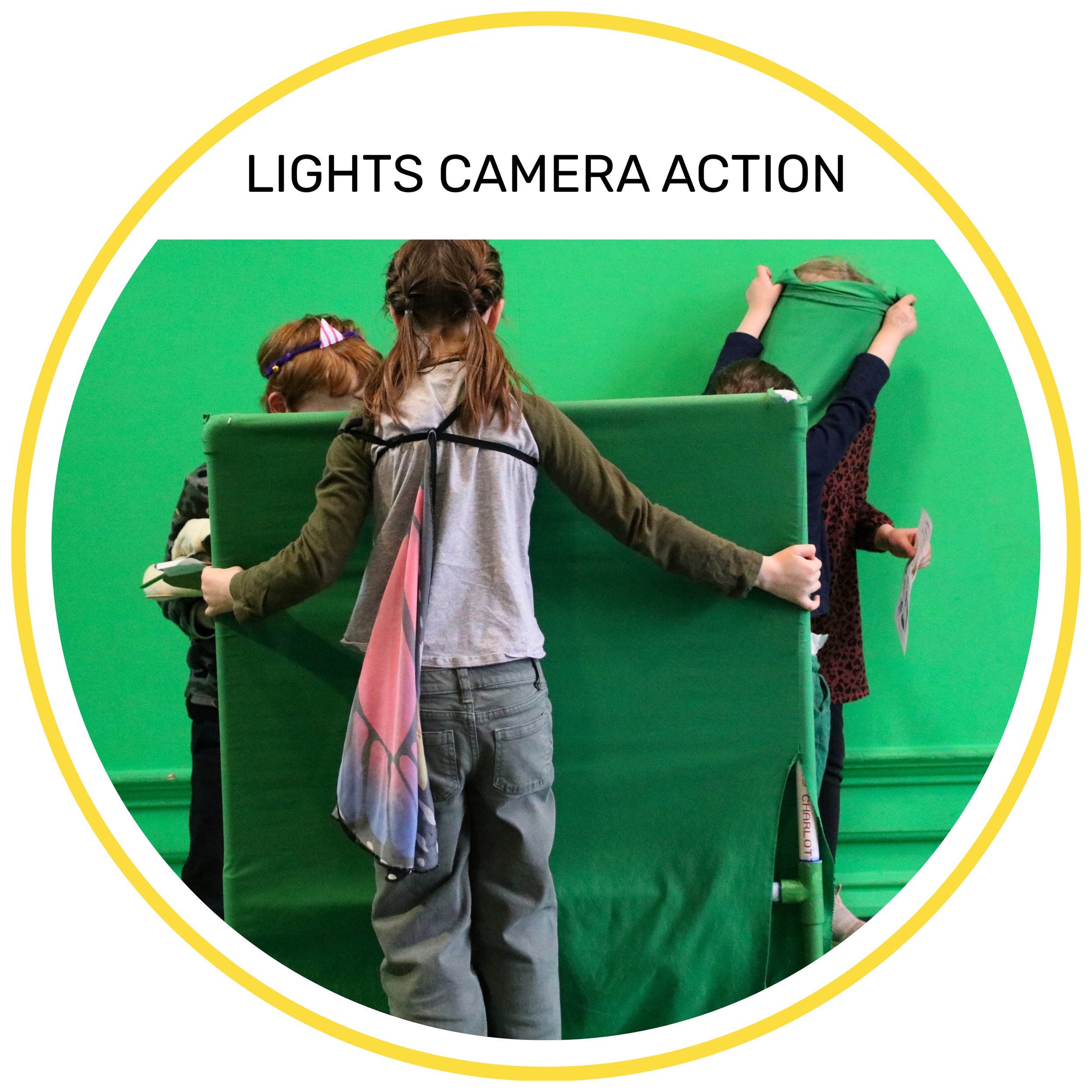 Two children standing in front of a bright green screen, using props for a video production activity.