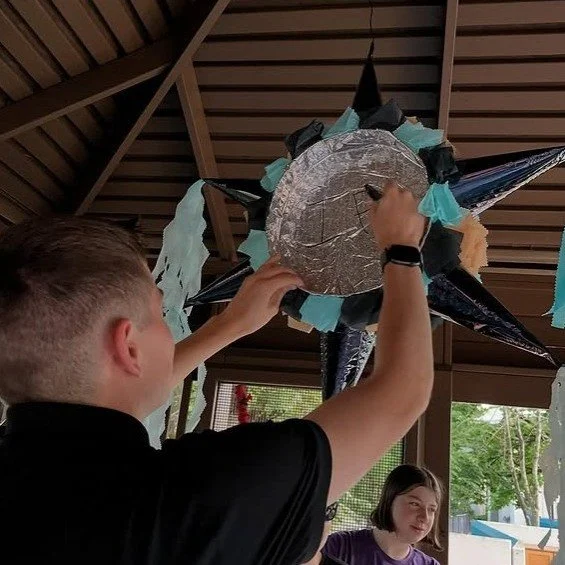 A graduate hangs up a star piñata in the museum gazebo during a private evening graduation party.