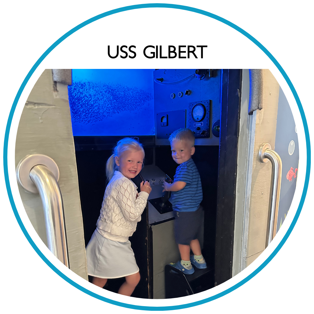 Two young children standing inside a blue, submarine-themed exhibit, looking at the dials and controls.