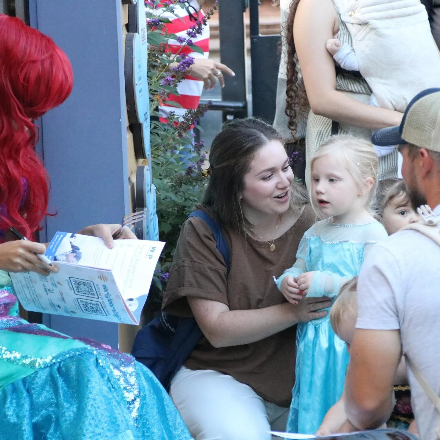 The Little Mermaid character signs a guidebook for a girl in an Elsa dress during a themed evening party.