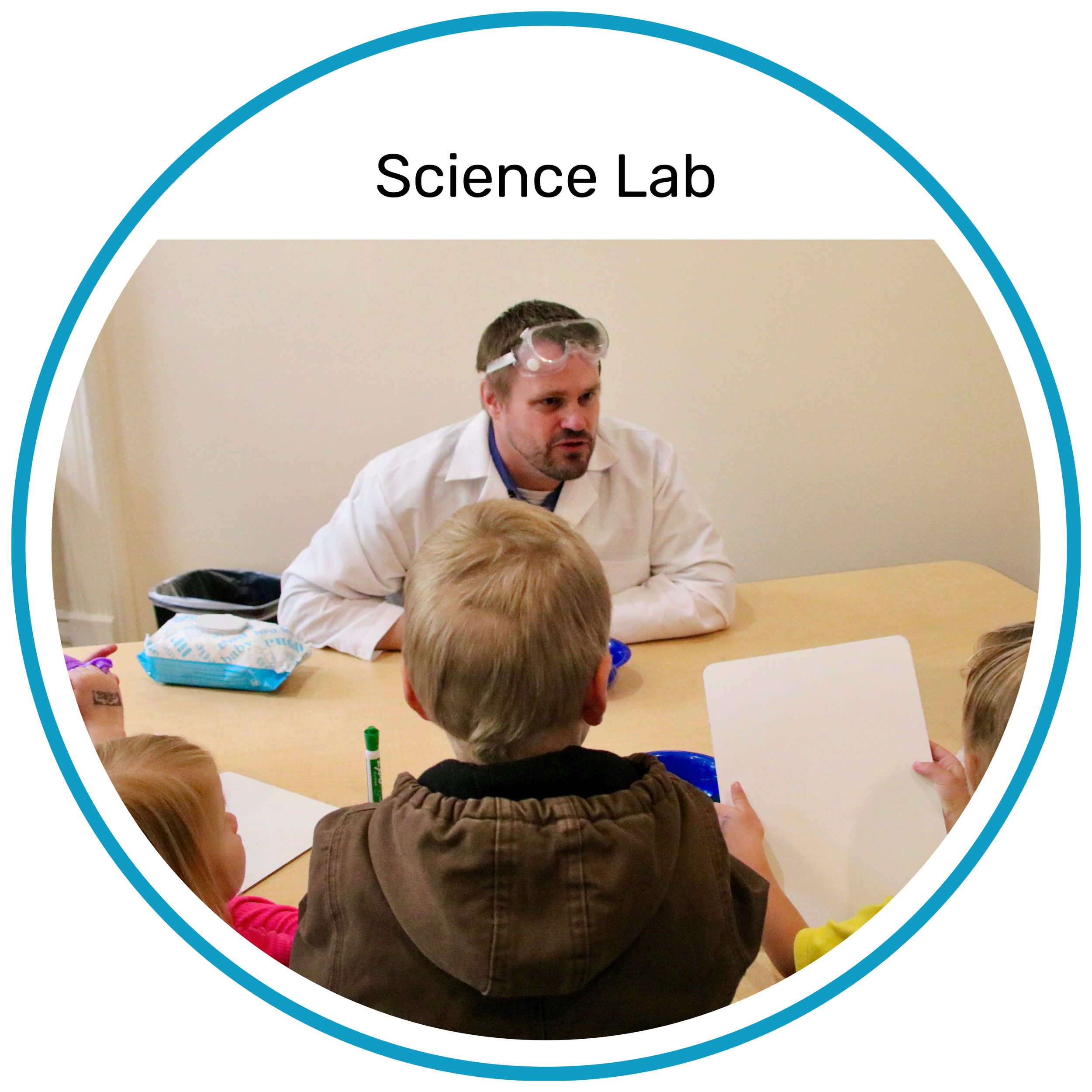 An adult instructor wearing a white lab coat helping two children at a table during a science activity.