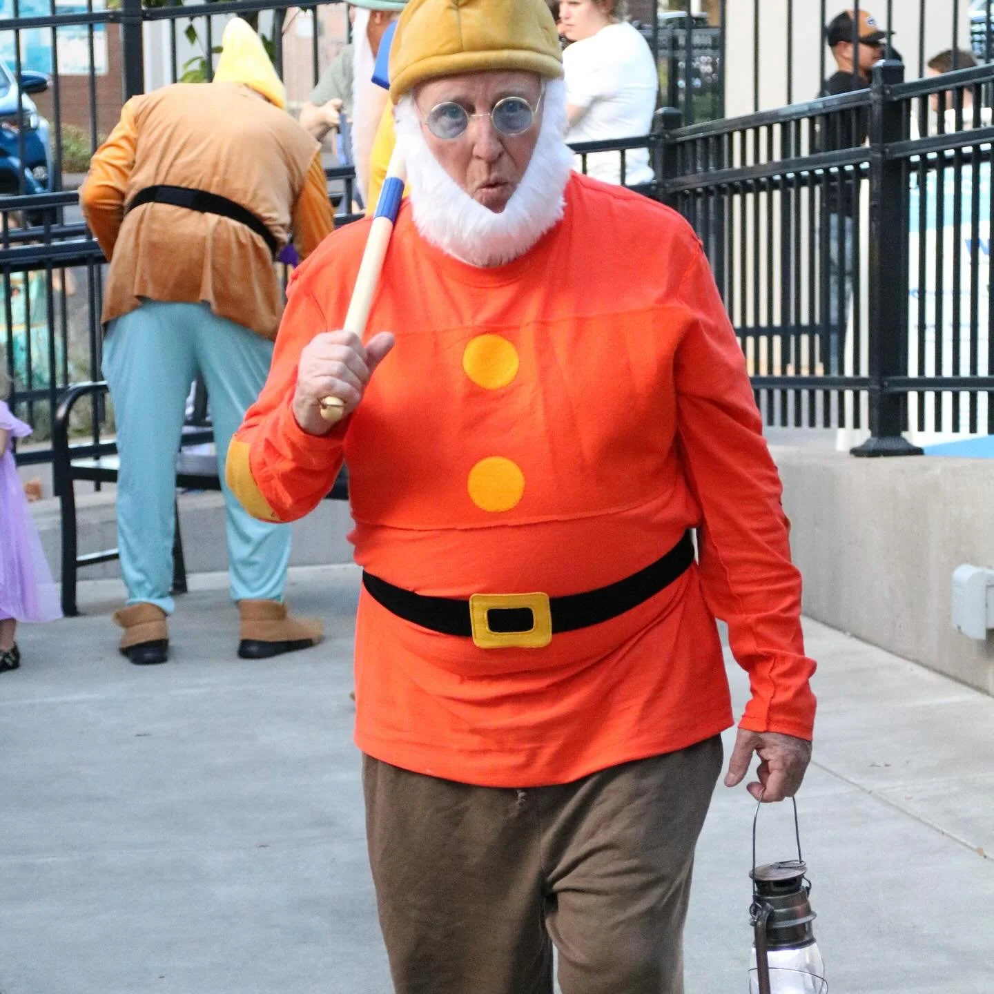 A man dressed as a dwarf character from Snow White walks with a lantern through the museum campus.