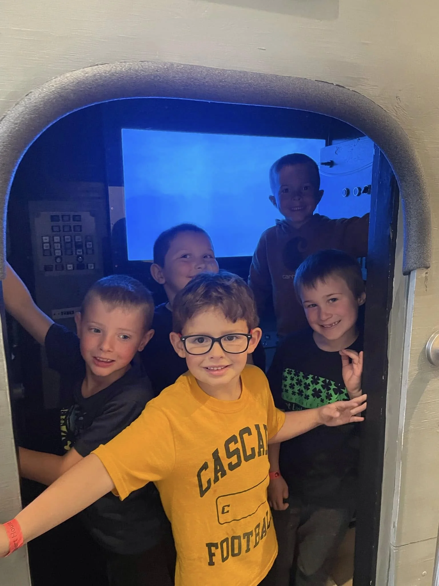 Six young boys smiling and posing for a photo inside a small room with a blue screen in the background.