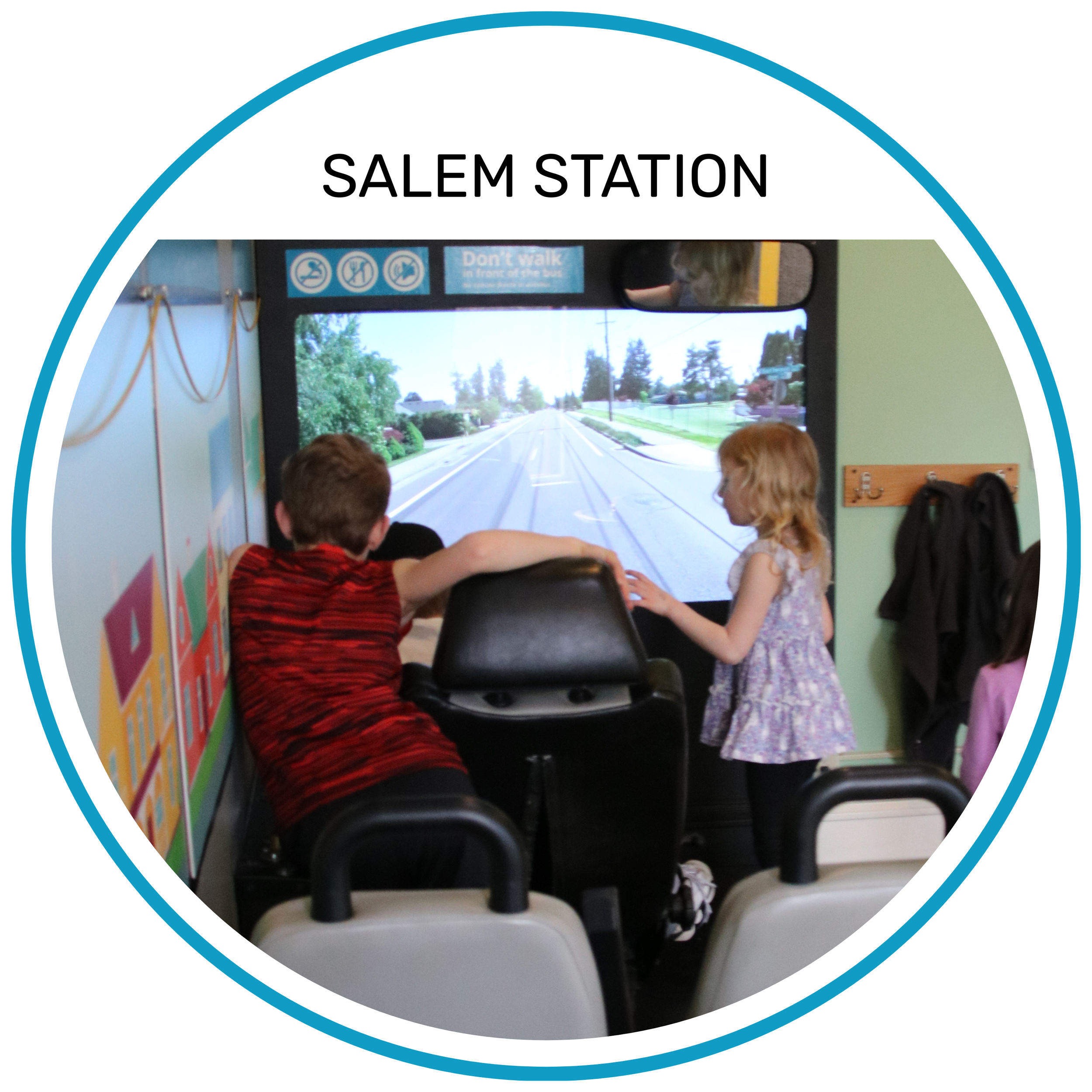 Two children riding the Salem Station bus simulator, with a large screen displaying a virtual street scene.