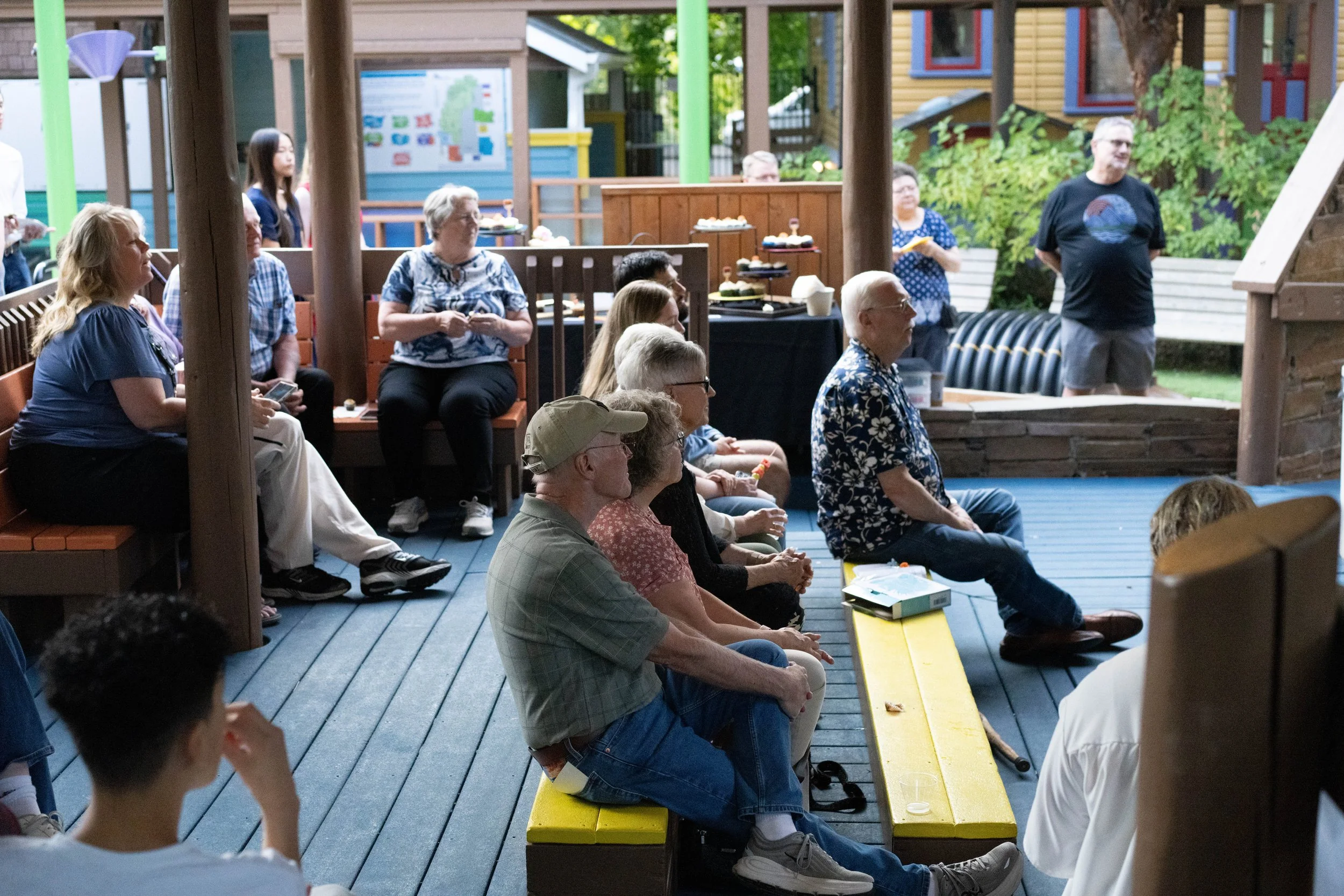 An intern giving a presentation about their mural project to guests seated in the museum's outdoor gazebo.