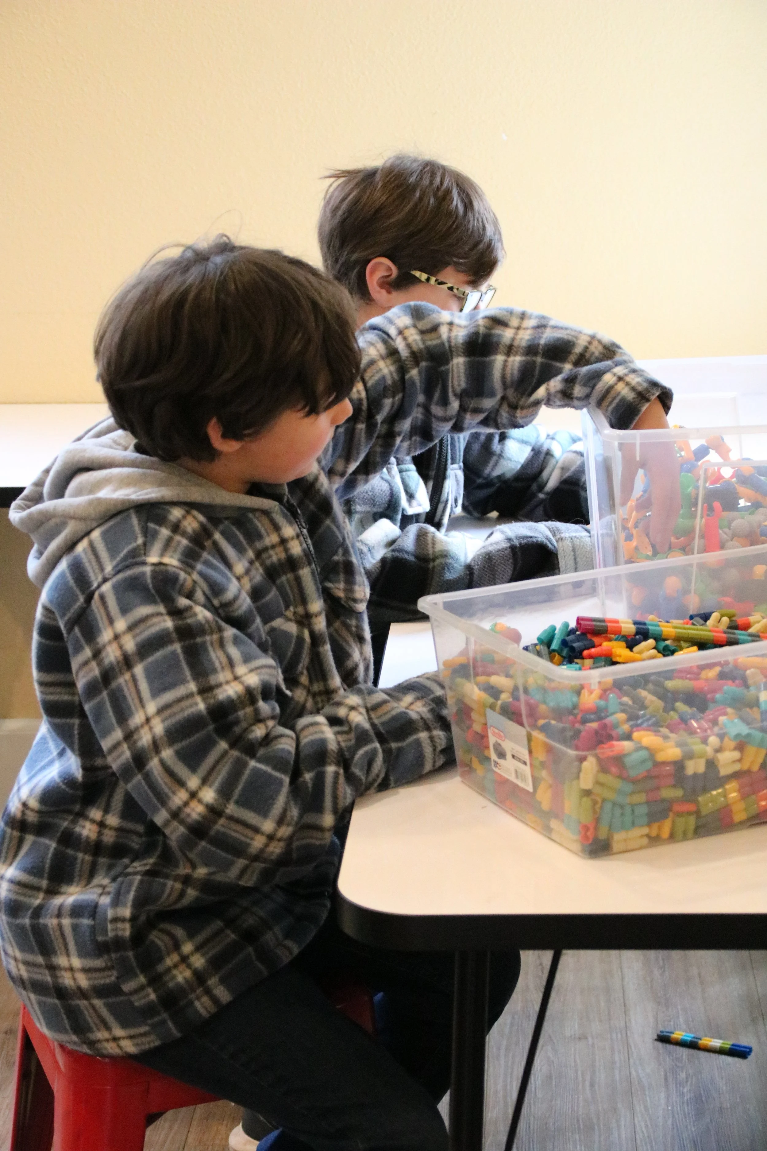 Two young boys with plaid shirts playing with colorful building blocks at a table.
