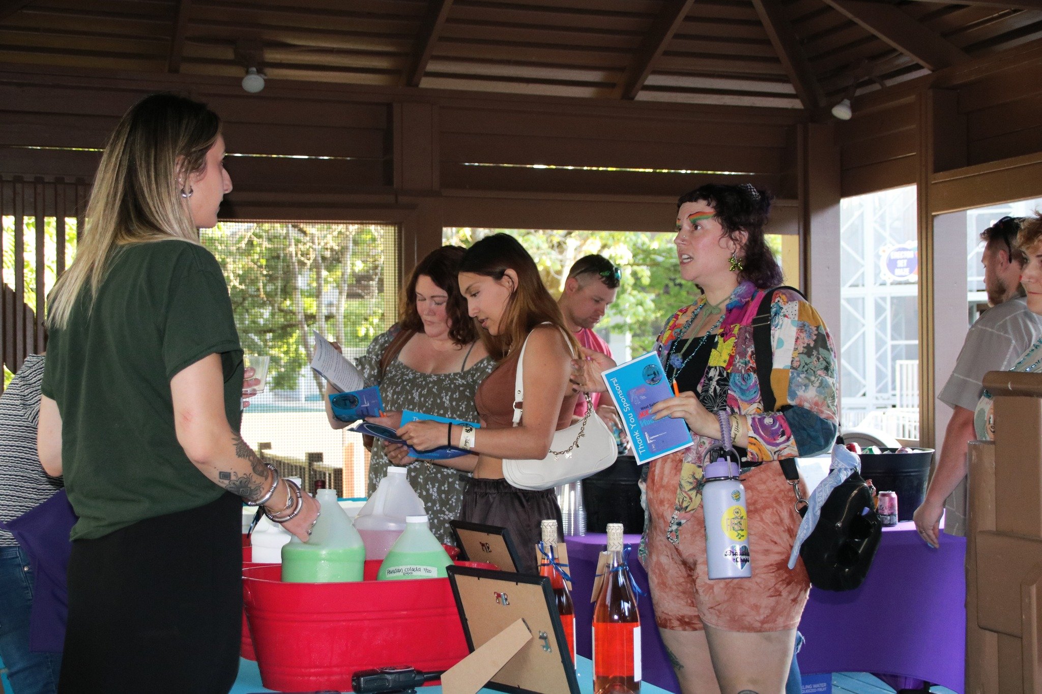 Group of people at an indoor event, engaging in conversation, with informational brochures and bottles on display tables.