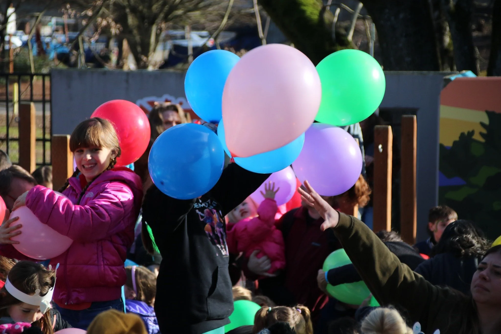 Children holding colorful balloons at an outdoor event on a sunny day.