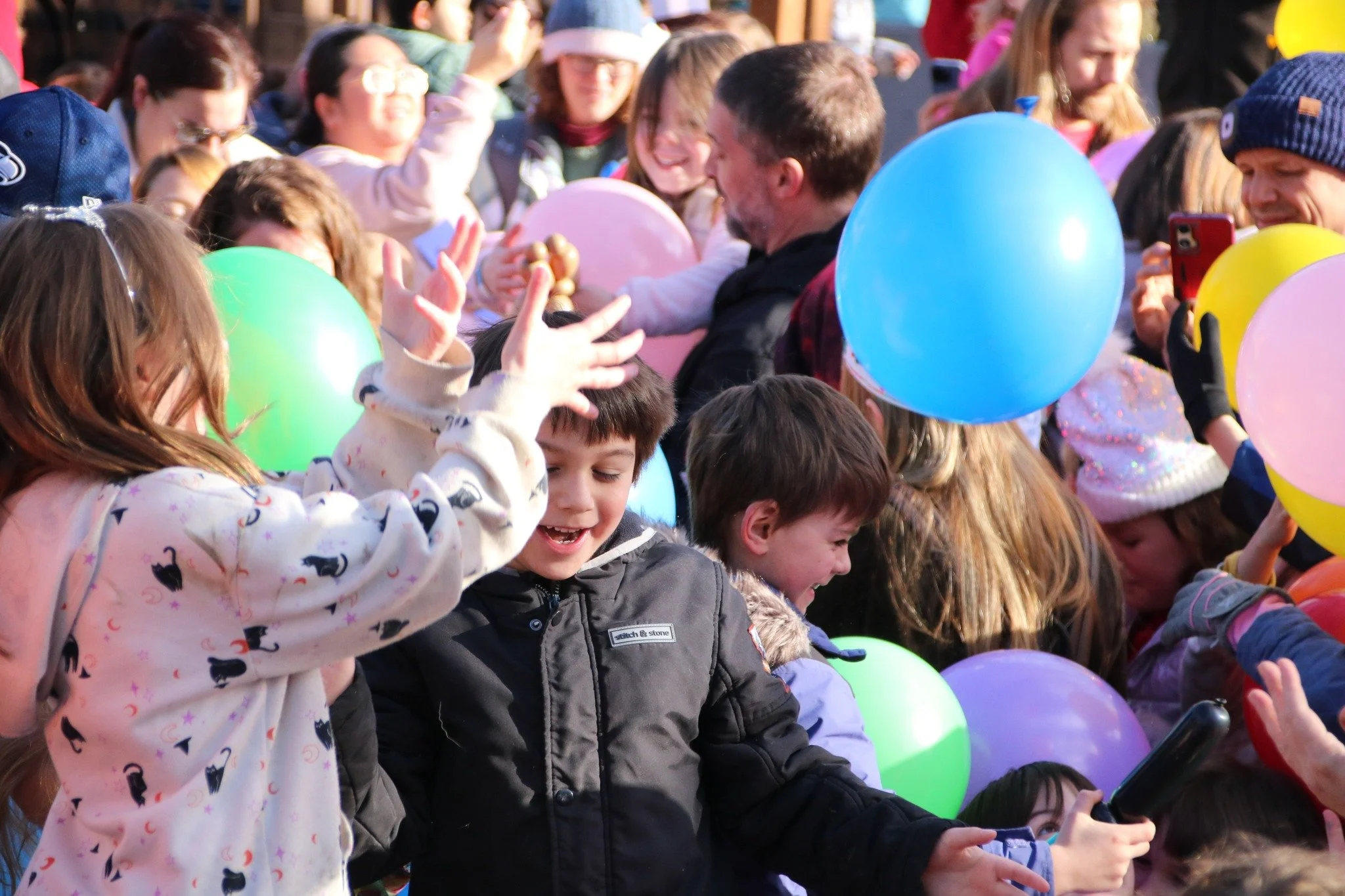 Children and adults celebrating with colorful balloons and smiling in a crowded outdoor event