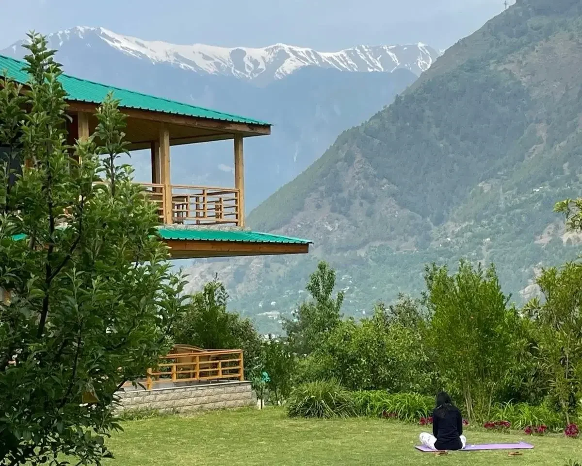 Spring detox in the mountains, lady sat on yoga mat near wooden cabin in mountain range