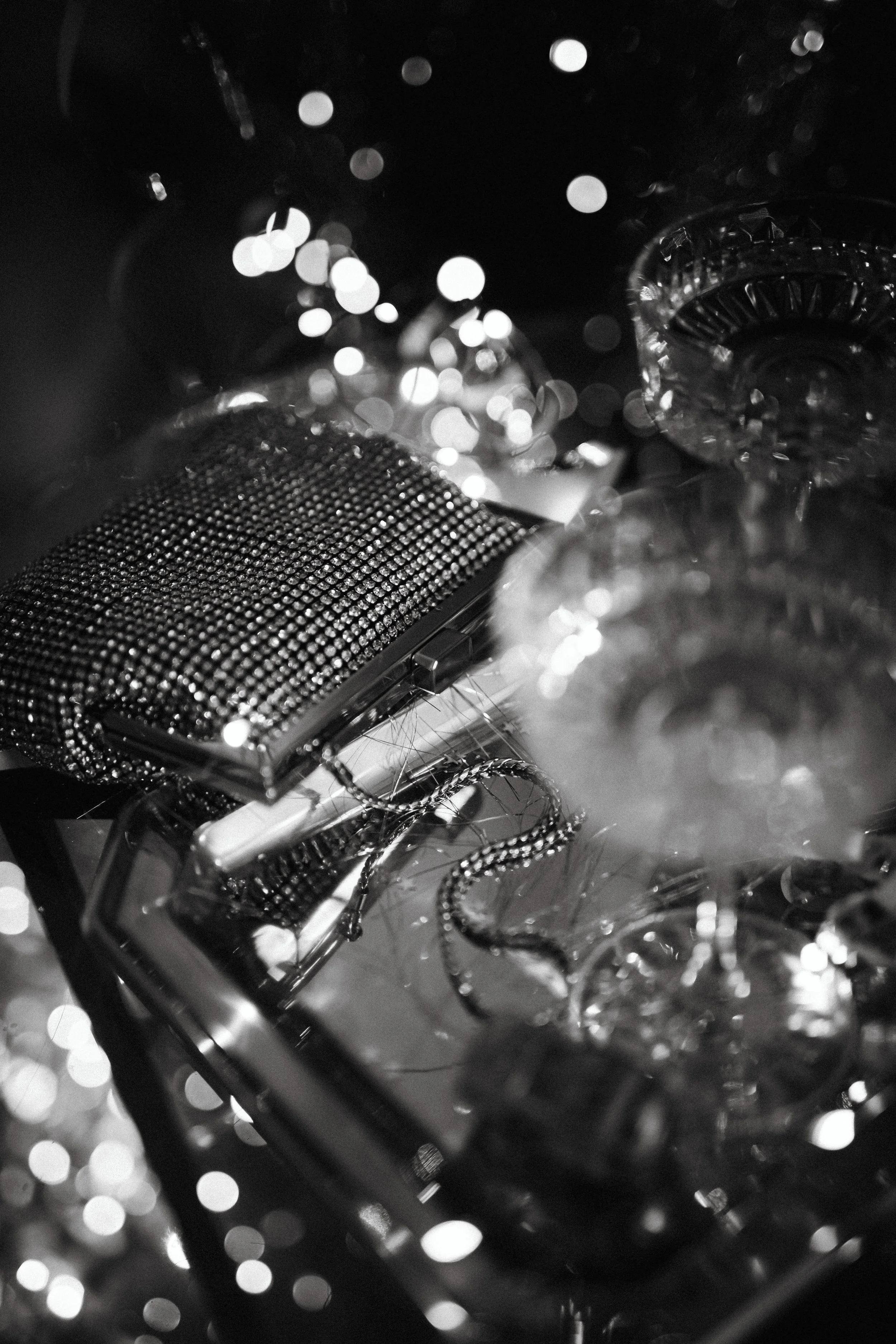 A collection of jewelry accessories, including a rhinestone clutch, necklaces, and glass vases, arranged on a table with out-of-focus bokeh lights in the background.