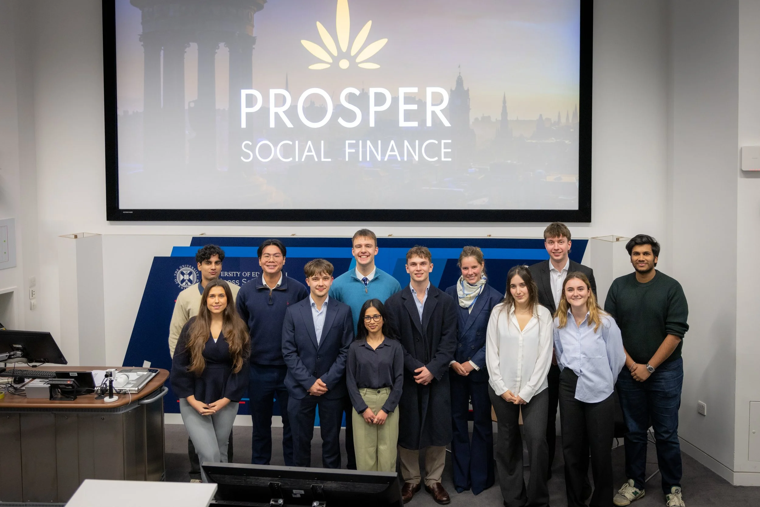 Group of young adults in a classroom with a large screen that reads 'PROSPER SOCIAL FINANCE.'