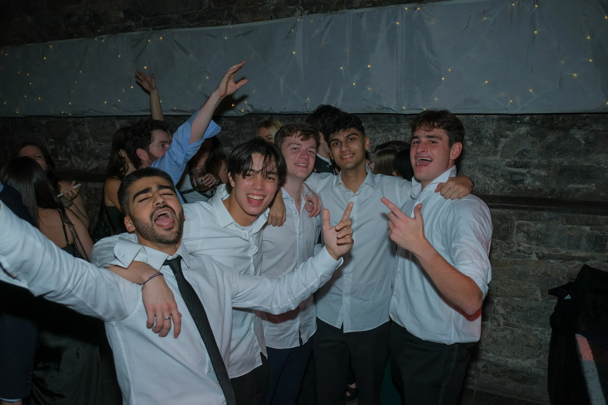 Group of young adults celebrating at a party, dressed in white shirts, smiling, and posing together.
