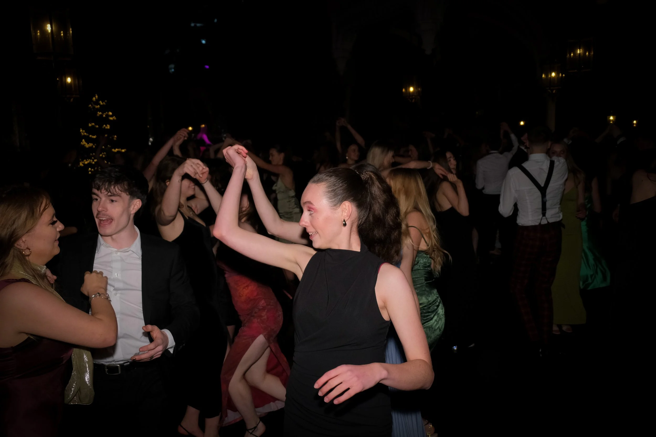 People dancing and socializing at a party or celebration in a dimly lit venue with holiday decorations.