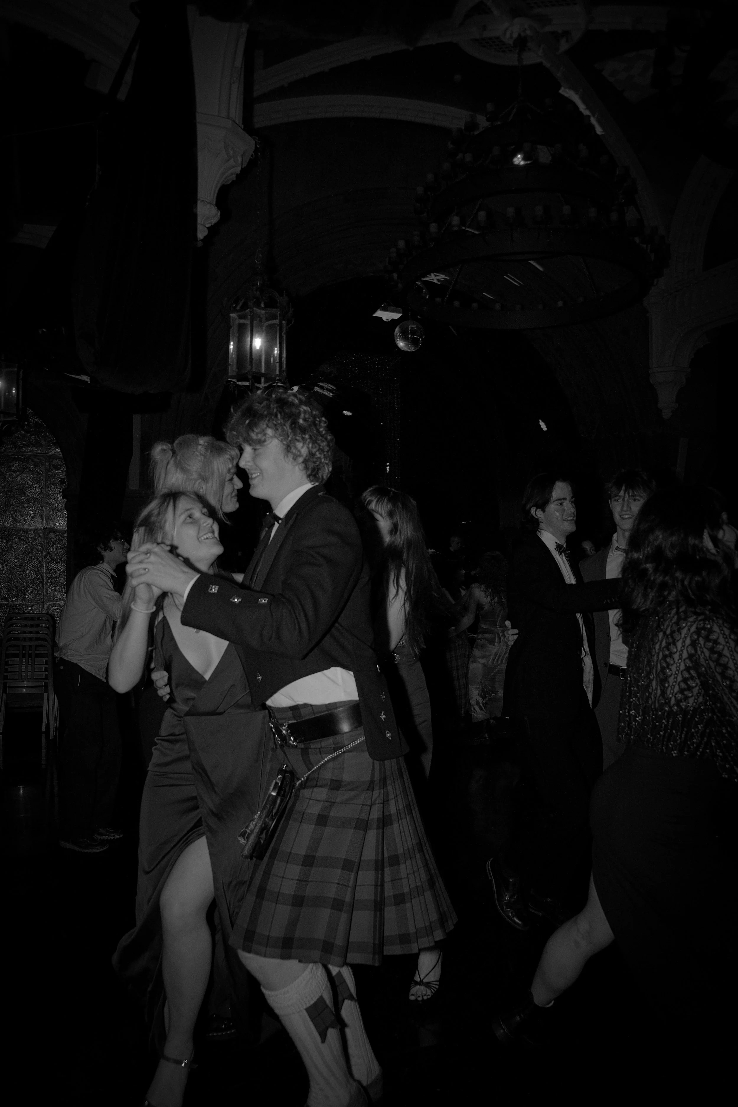 Couple dancing and smiling at a party with other people dancing in the background.