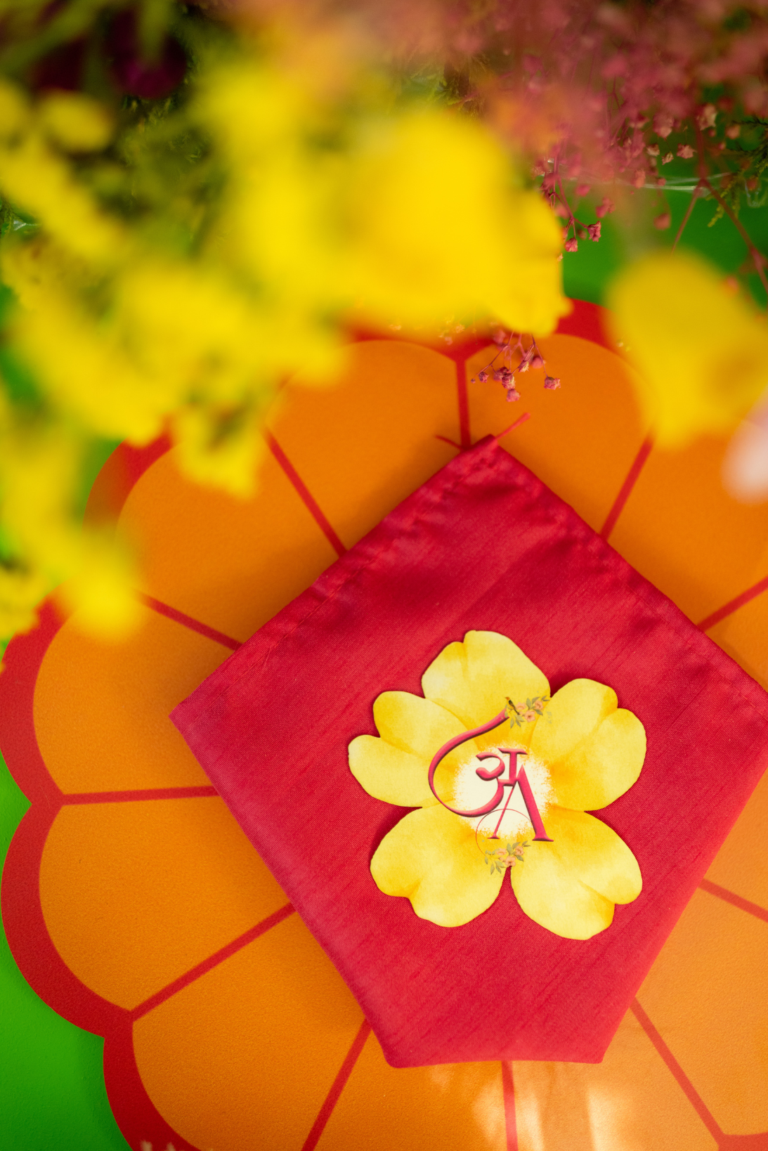 Close-up of a decorative setting with a red napkin, yellow flower design, and a background of orange and yellow flowers.