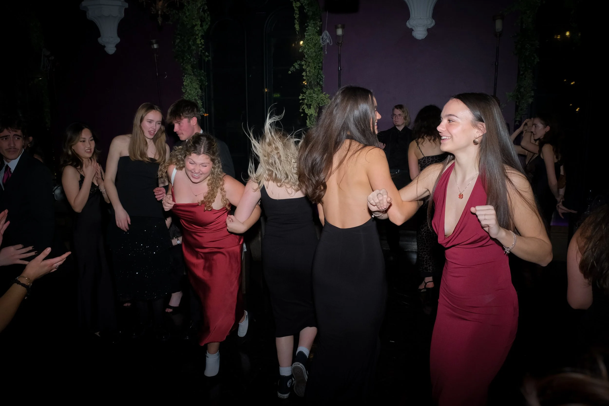 People dancing and enjoying themselves at a party or prom in formal attire, smiling and holding hands.