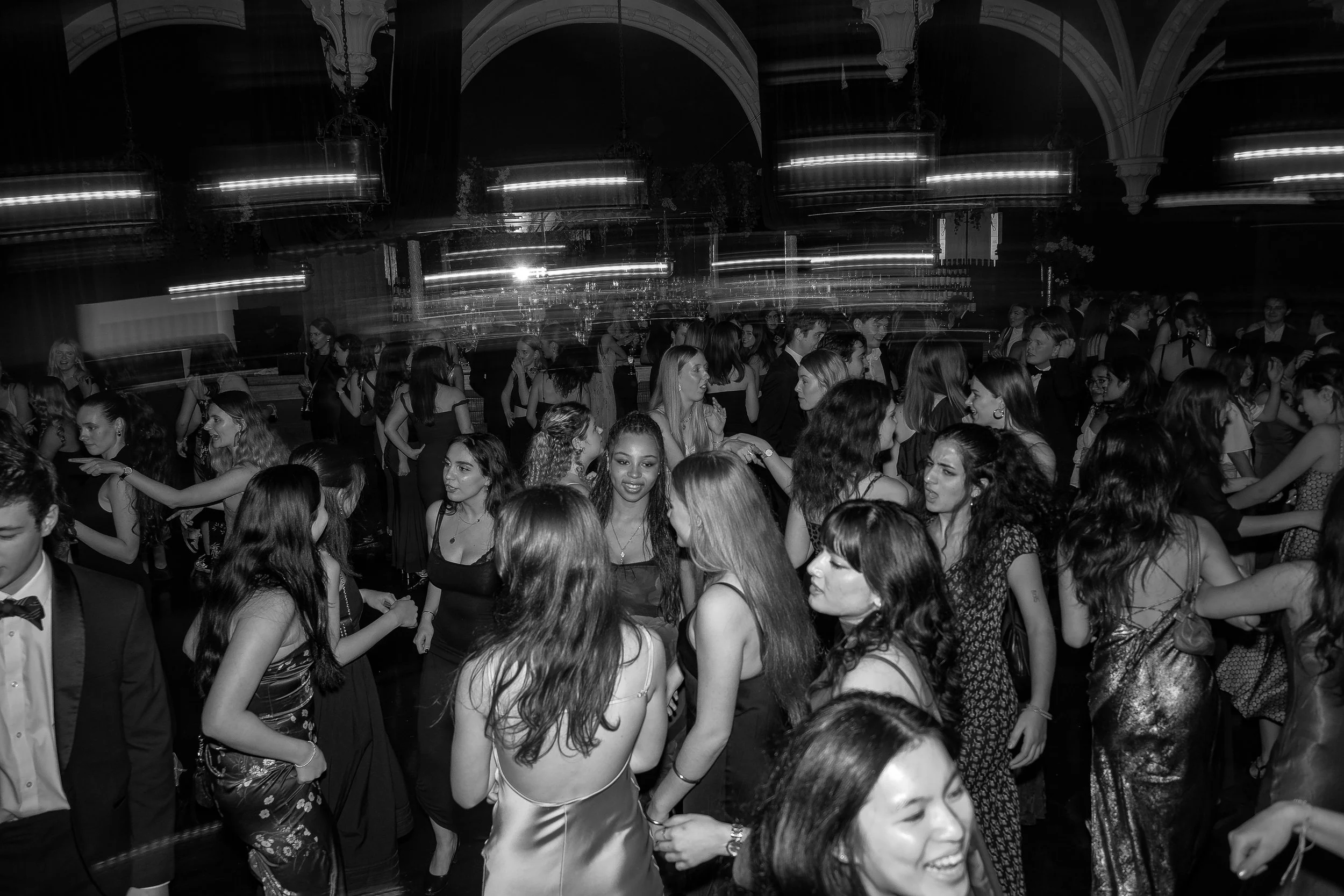 Young people dancing at a lively indoor party or dance event, dressed in formal and semi-formal attire.