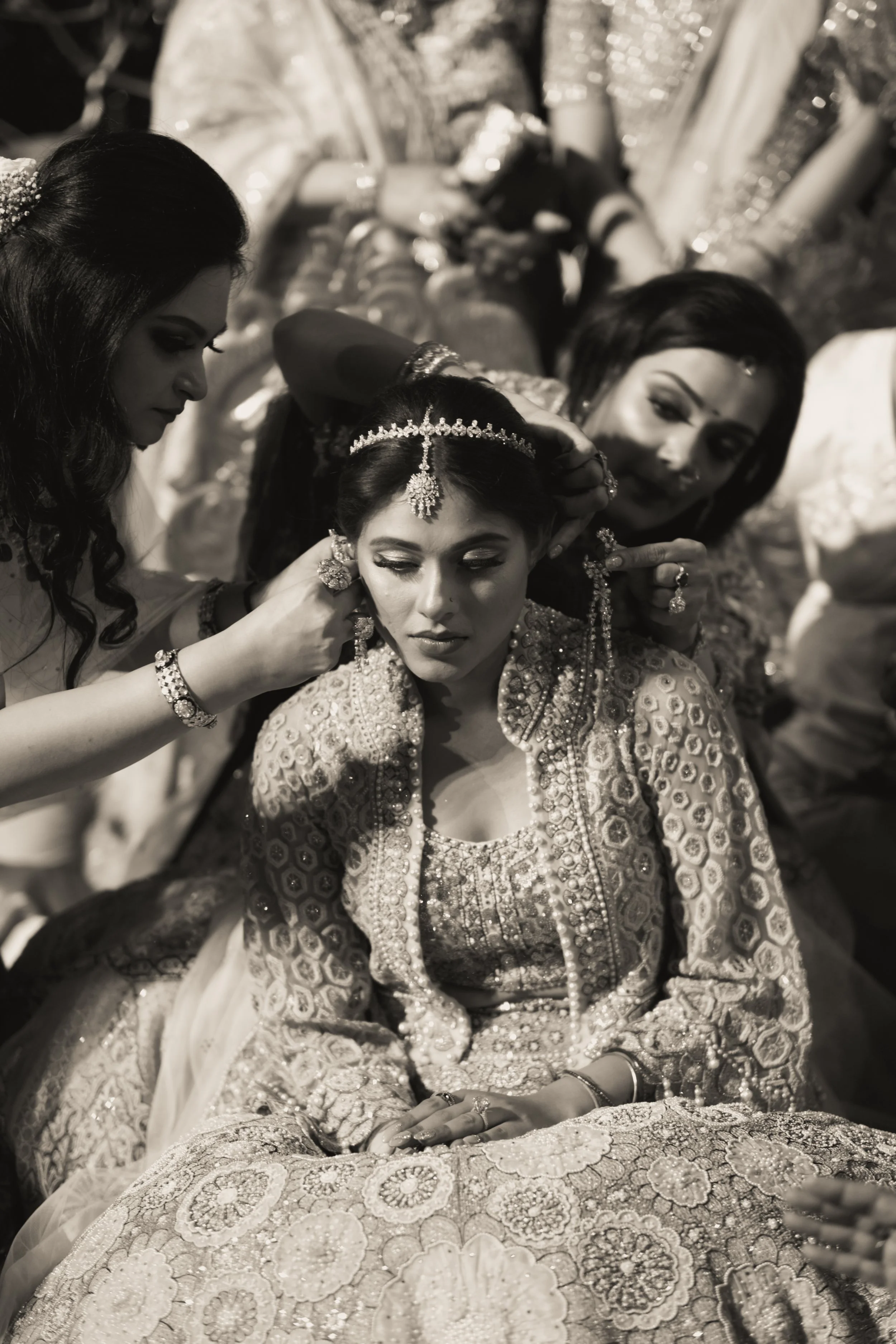 A bride being adorned with jewelry by women around her in traditional wedding attire, during a ceremonial moment at a wedding.