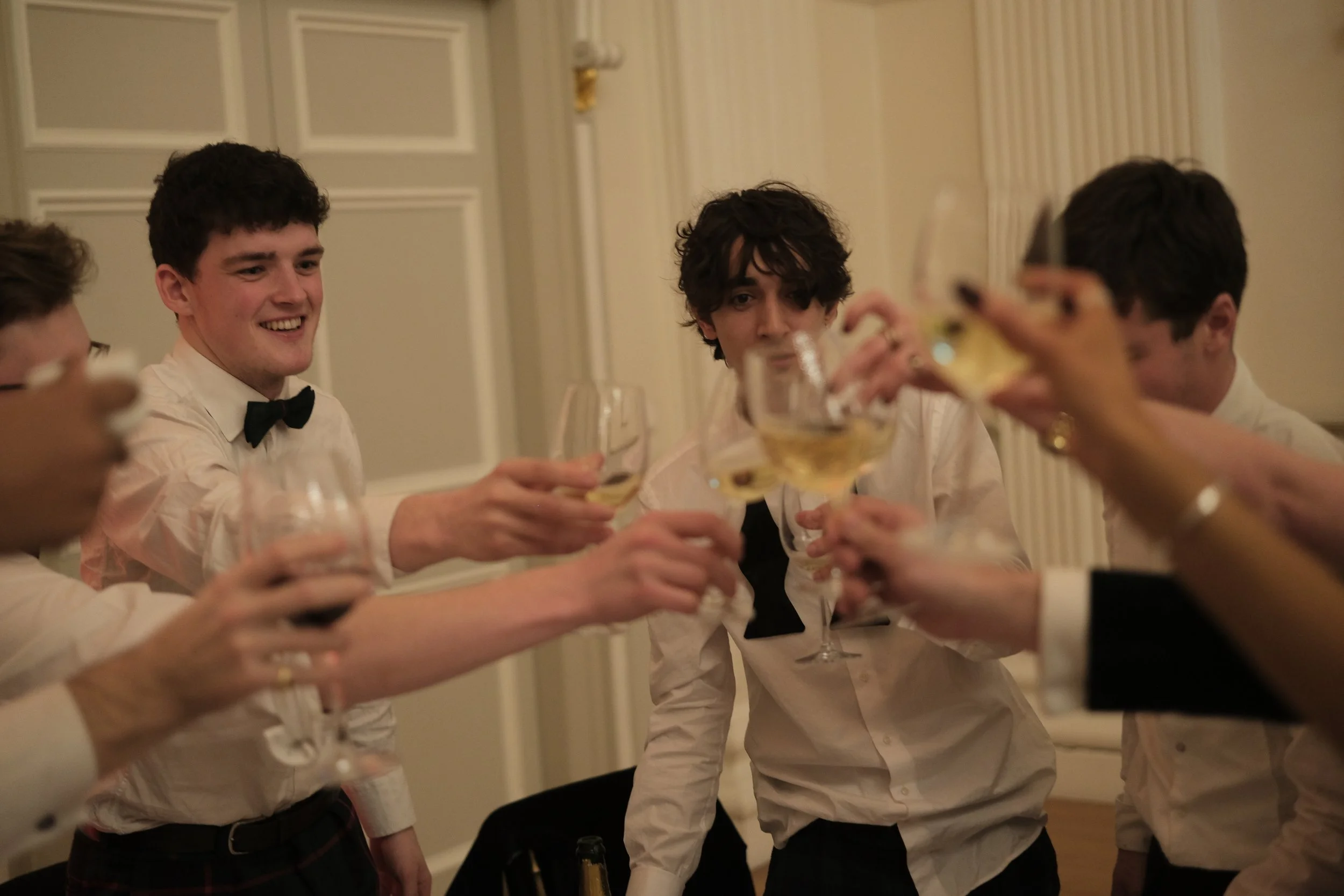 Group of young men in formal attire raising glasses for a toast at a dinner party.