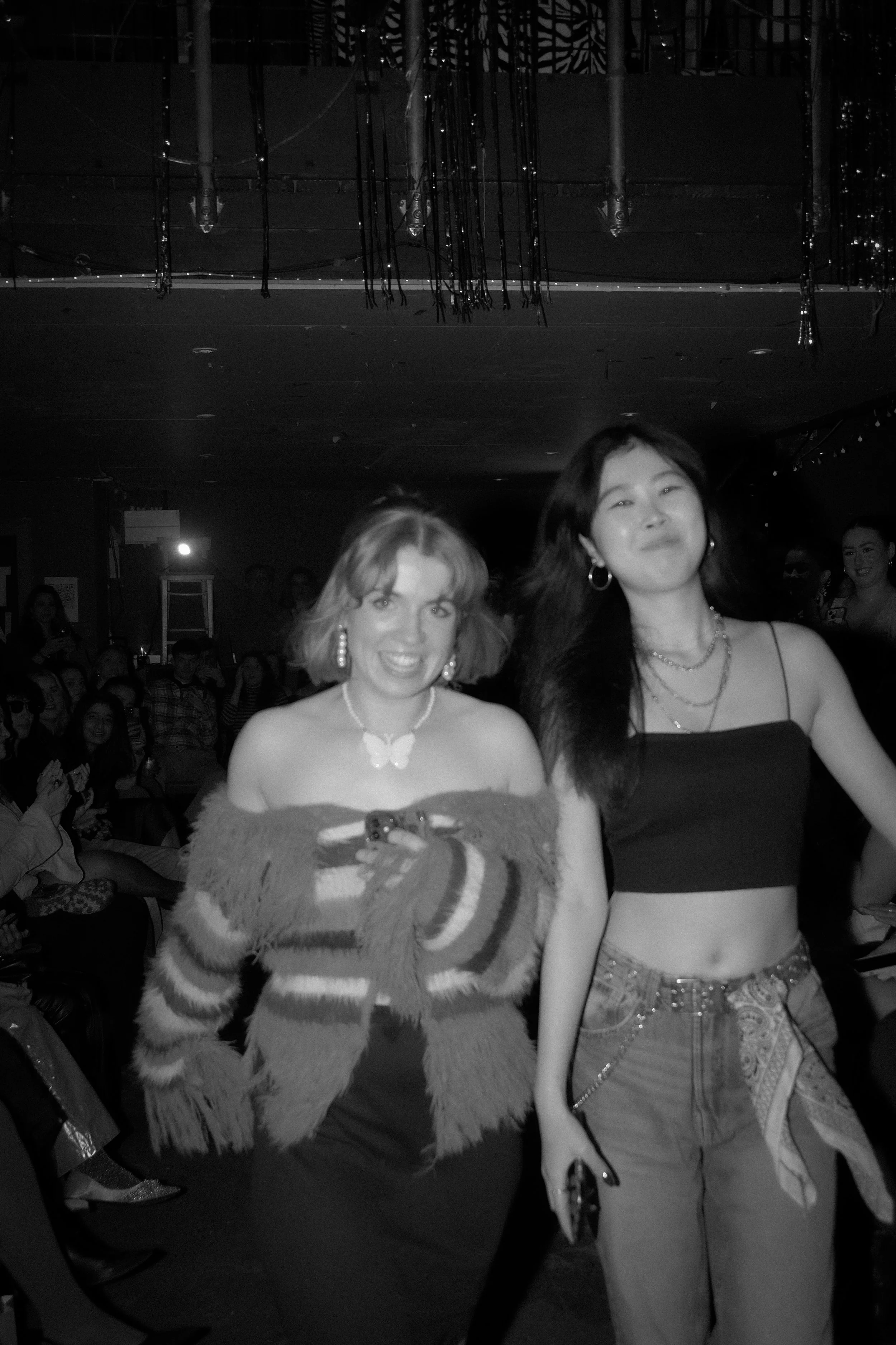 Two women walking and smiling at an event, with the audience in the background.