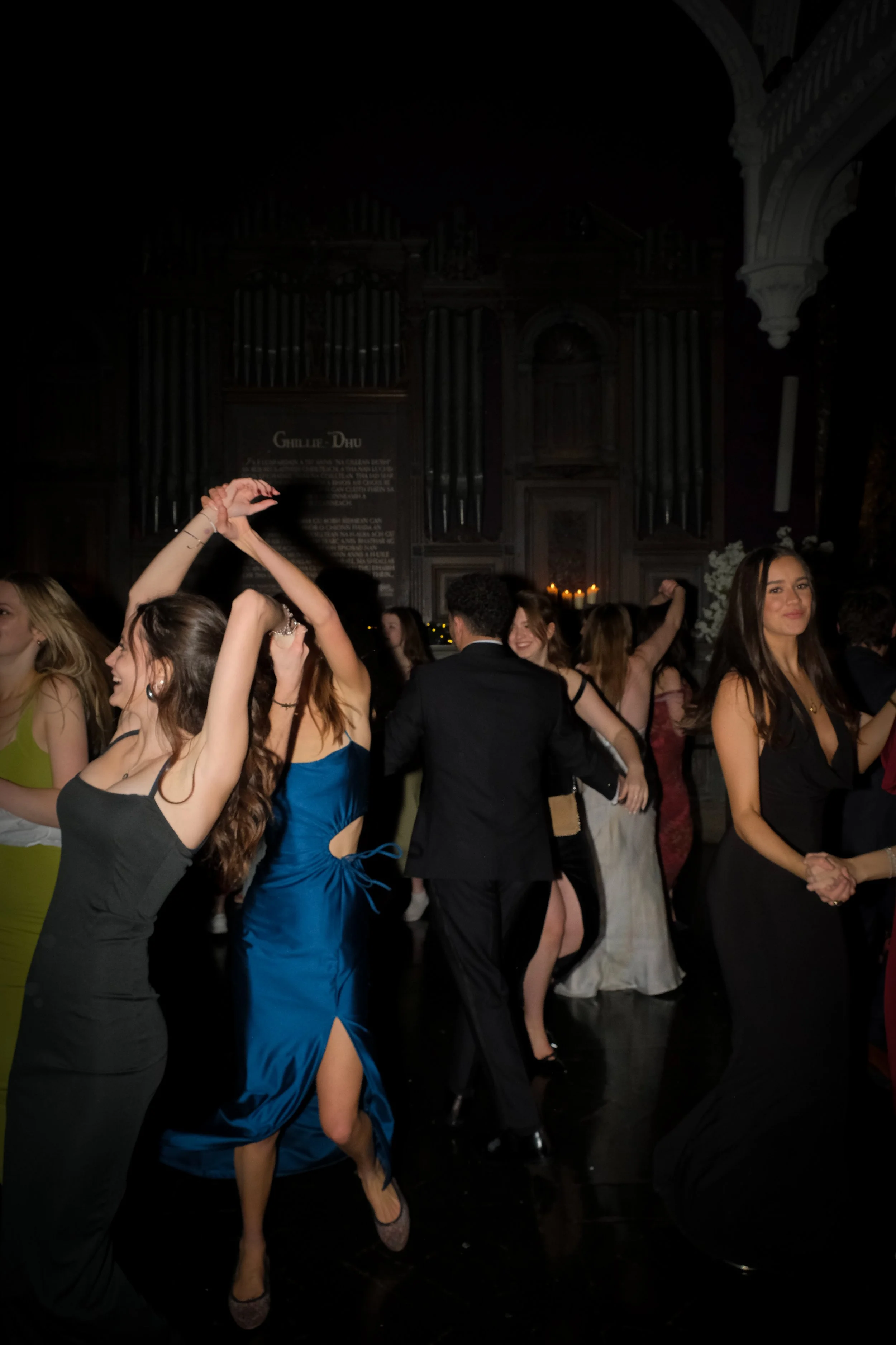 Group of young people dancing and socializing at a formal event in a dimly lit hall.