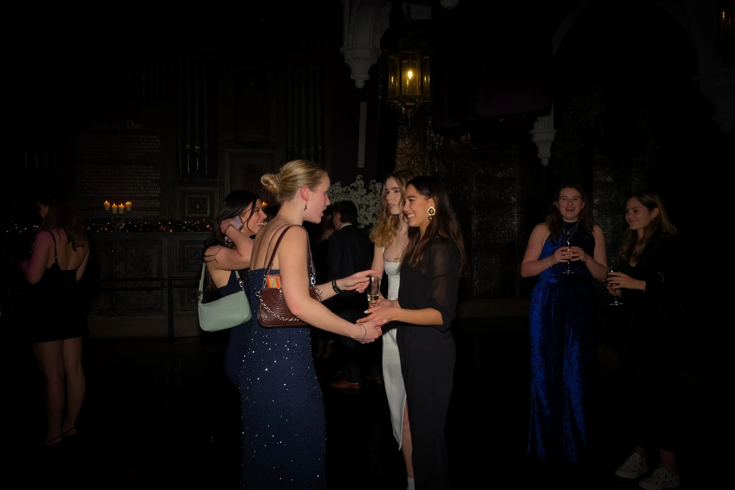 Group of young women in evening dresses socializing and exchanging drinks at a nighttime party.