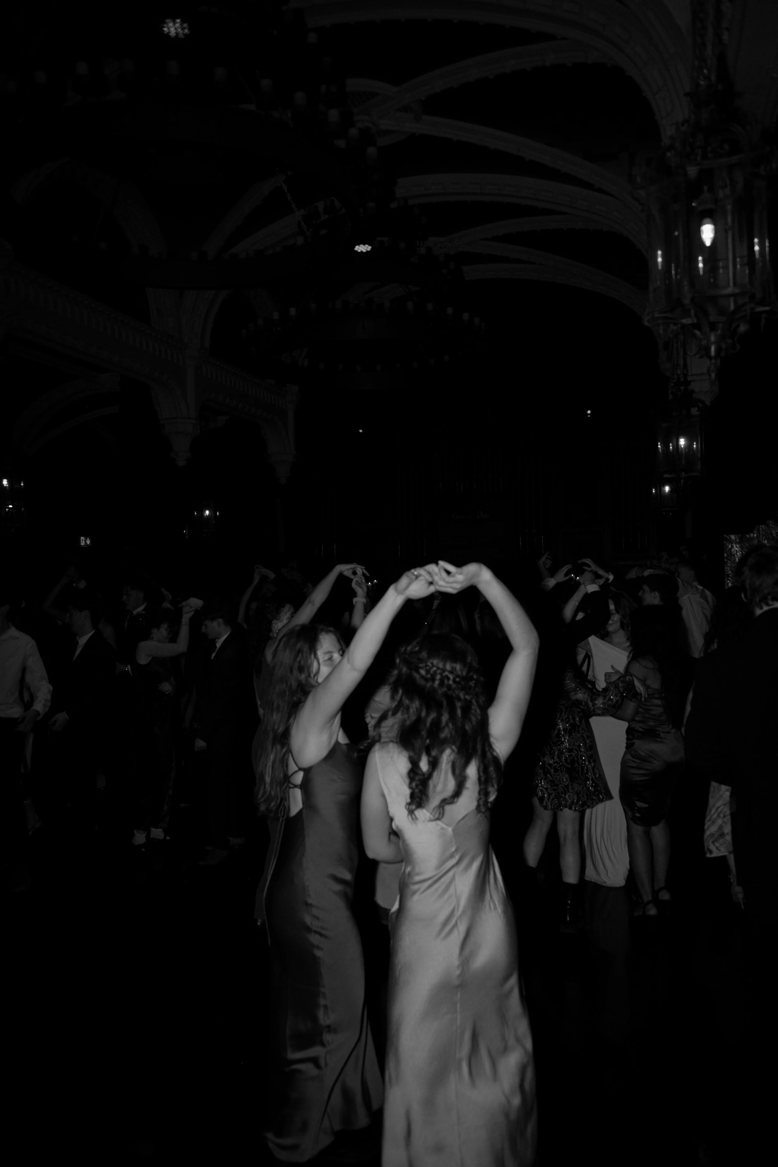 Two women dancing at a formal event with other people dancing in the background, in an ornate ballroom.