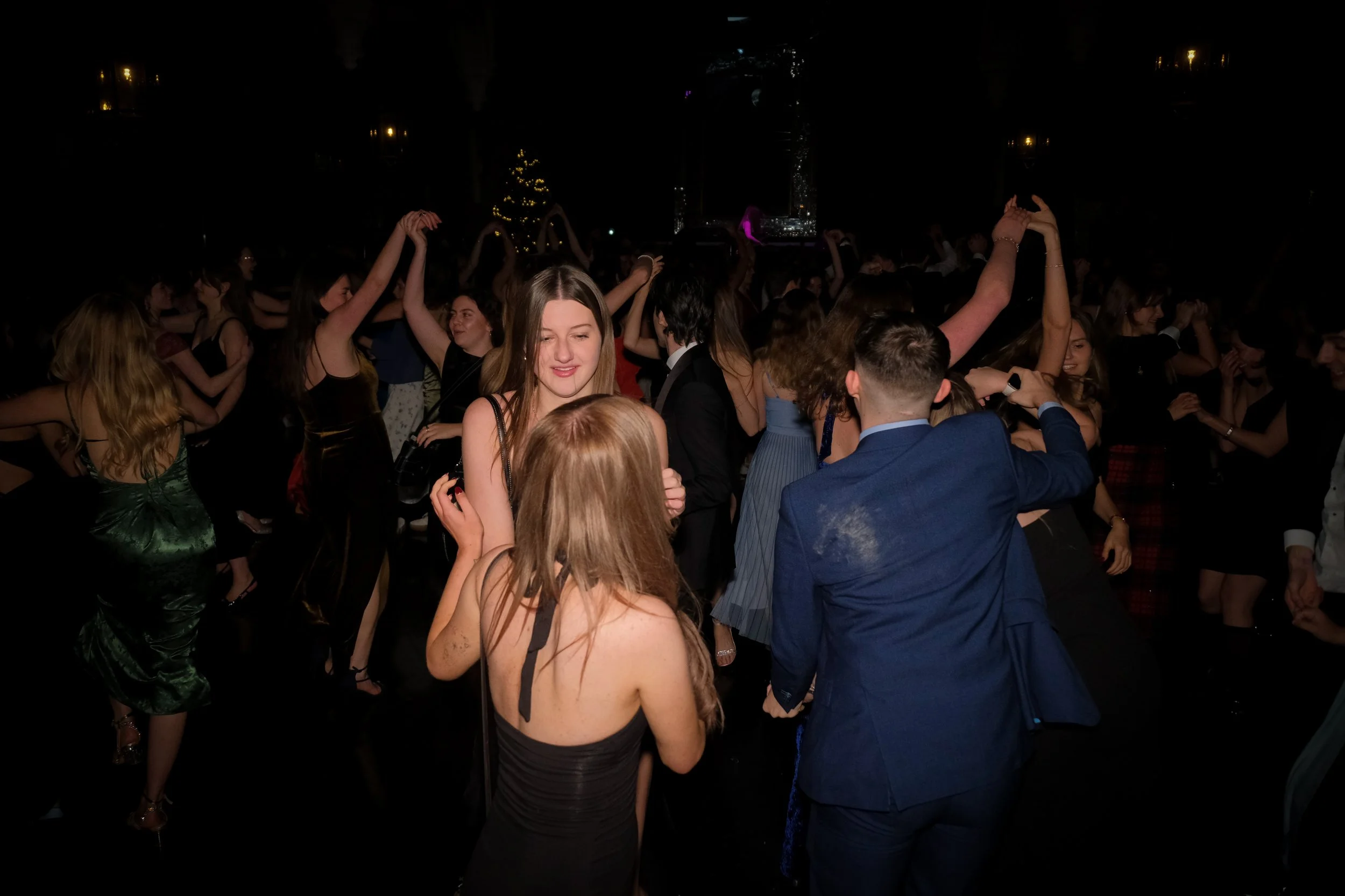 Fairy-tale themed ball or dance party with people dancing and socializing, decorated with Christmas trees and festive lighting.