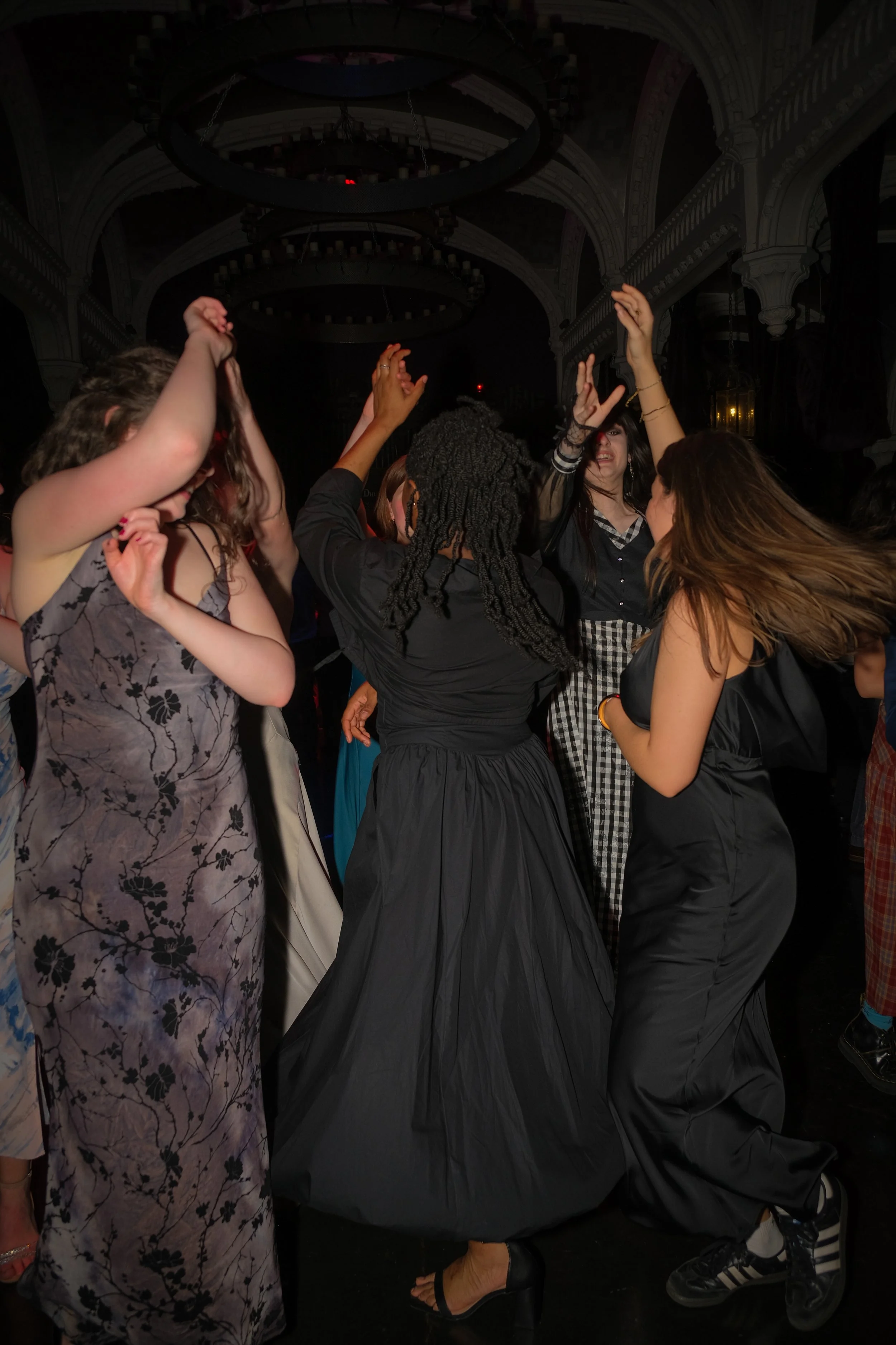 A group of women dancing at a party in a dimly lit, ornate room.