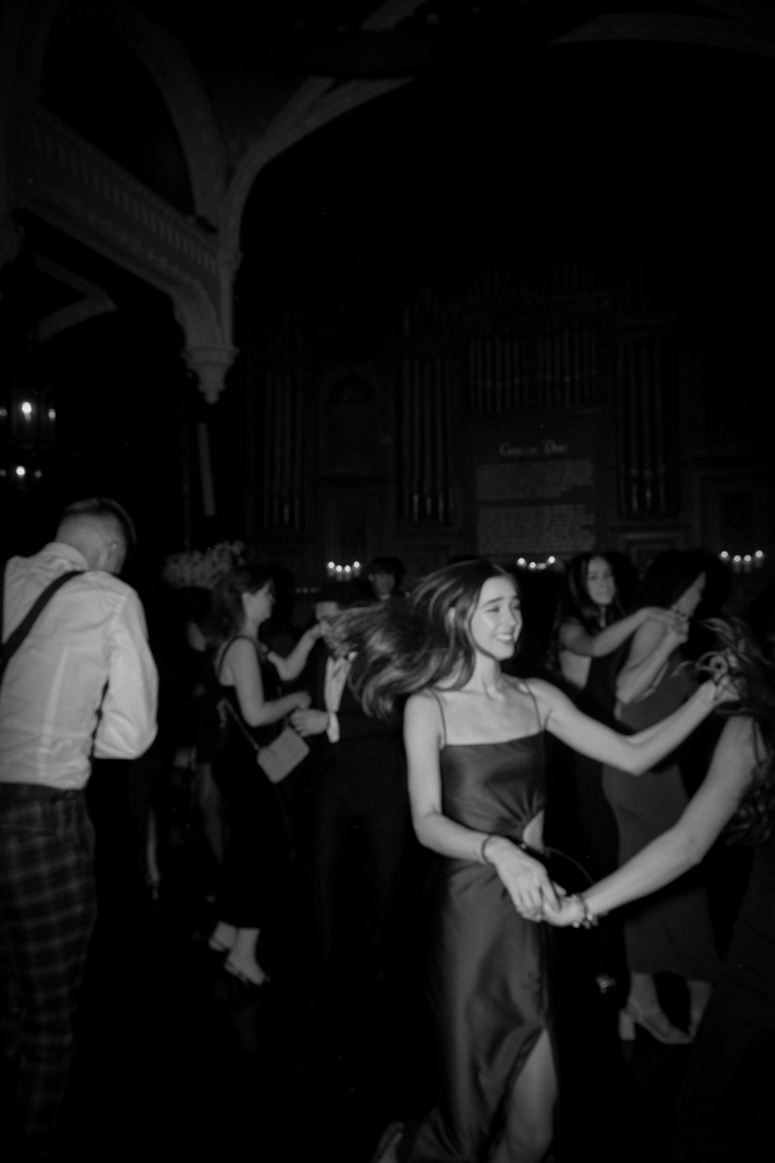 People dancing at a party or club, smiling and holding hands, in a dimly lit indoor setting.