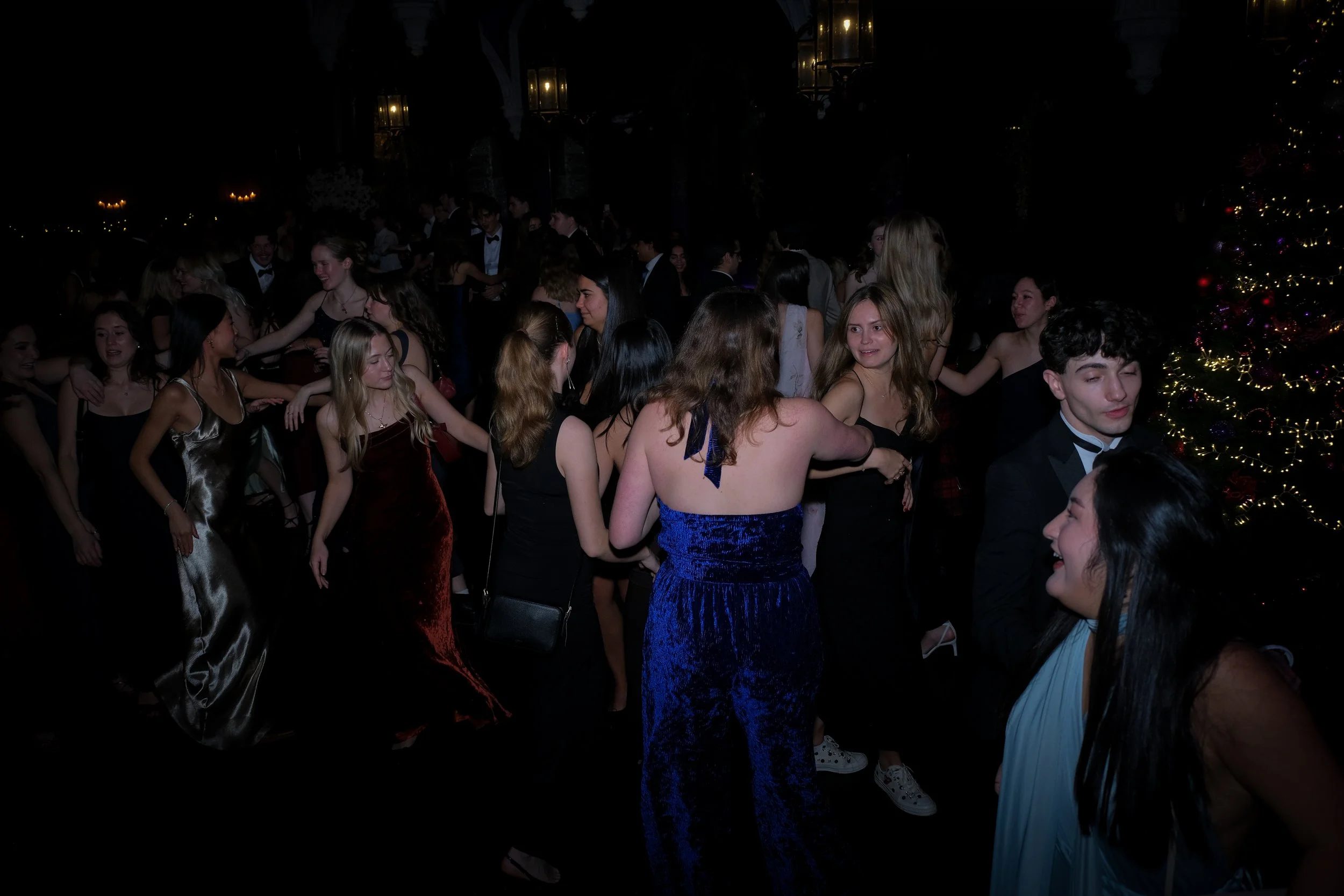 A group of young people dancing at a festive party, with Christmas lights and a Christmas tree visible in the background.