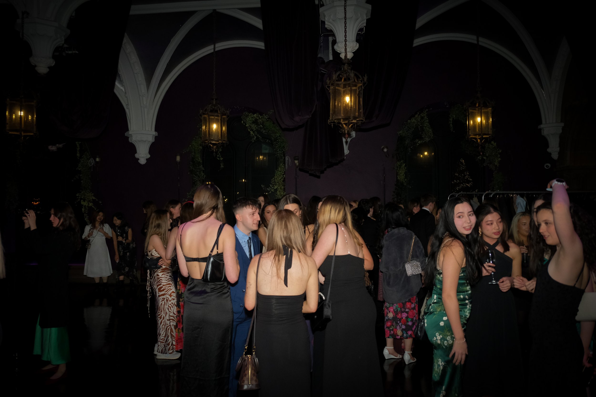 People dancing and socializing at a party or nightclub with dark walls, chandeliers, and decorative lighting.