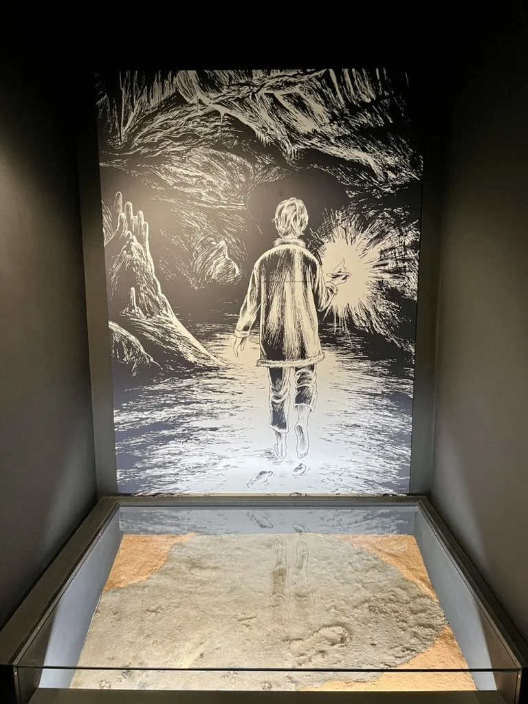 An illustration of the painter walking through the caves, above a recreation of the footprint found inside