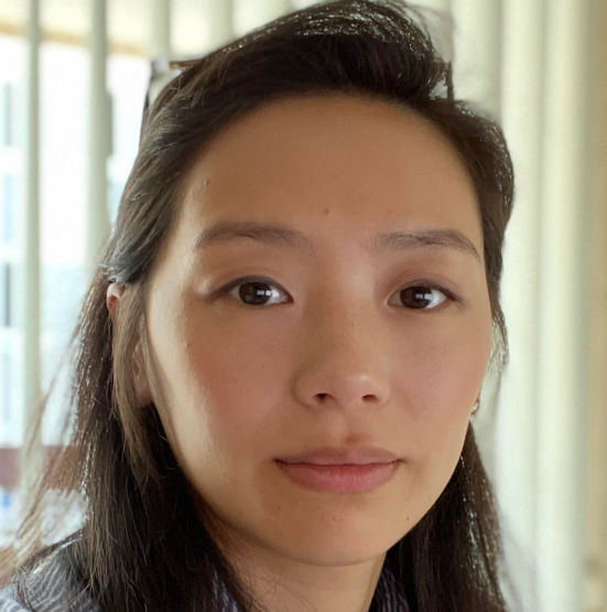 Close-up of a young woman with dark hair and light skin, indoors with natural light.