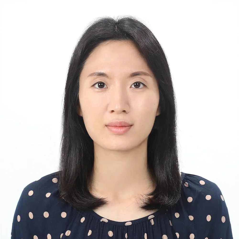 Portrait of a woman with shoulder-length black hair wearing a navy blue top with pink polka dots against a white background.