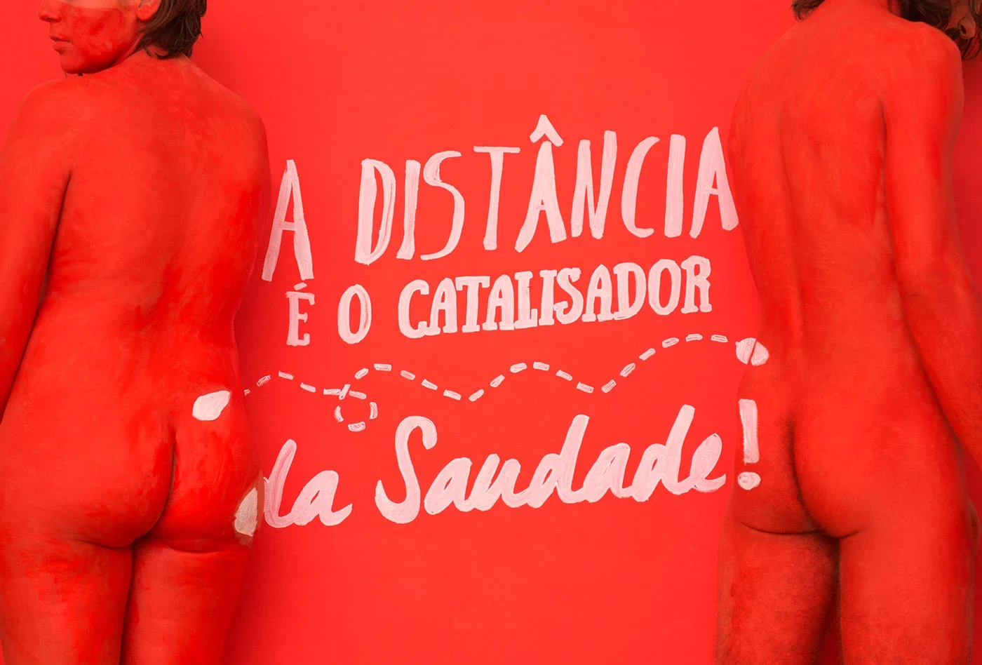 Dois corpos humanos de costas, parcialmente visíveis, com a pele pintada de vermelho, ao lado de uma parede vermelha com a frase em português 'A distância é o catalisador da saúde!' escrita em branco.