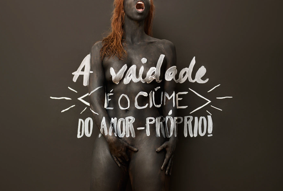 Pessoa com corpo pintado de preto, cabelo castanho e expressão de grito, com mensagem escrita na imagem: "A vaidade é o cúmulo do amor próprio!"
