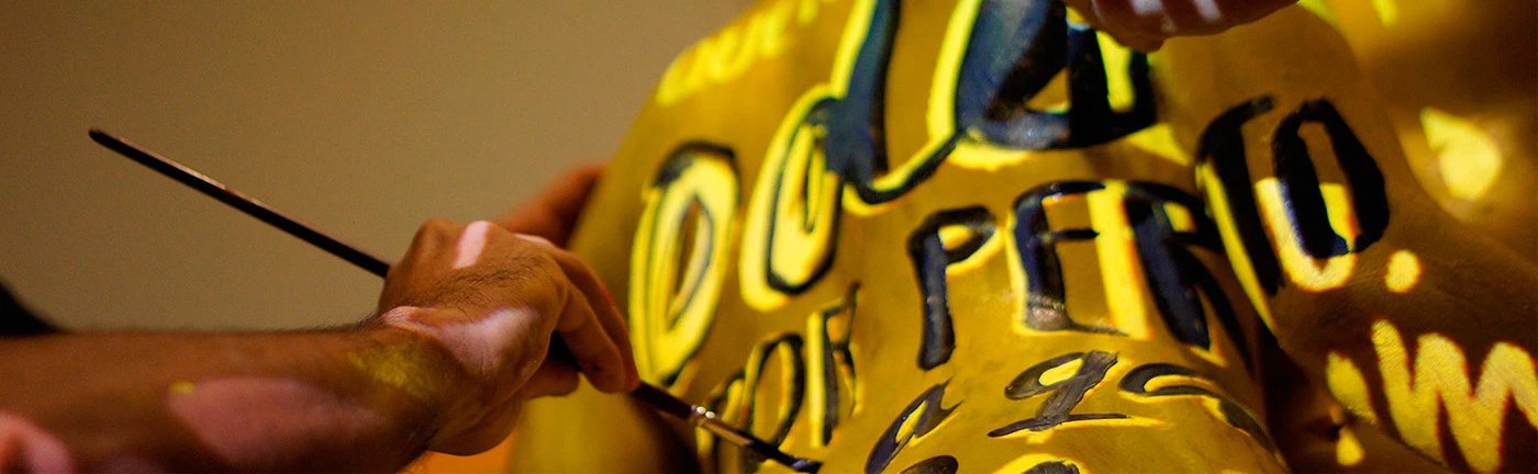 Pessoa pintando um escultura com letras e números em tons de amarelo e preto.