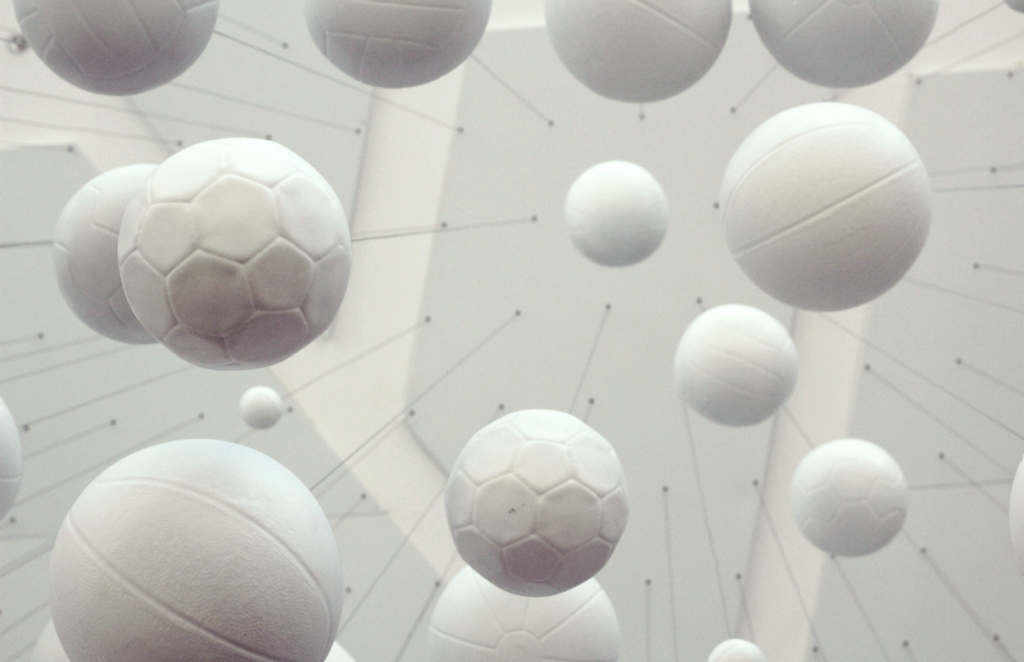 Vários objetos esféricos brancos de diferentes tamanhos flutuando. Alguns parecem bolas de futebol, outros semelhantes a bolas de tênis ou de basquete, suspensos em uma estrutura de rede no teto, em um ambiente com iluminação suave.