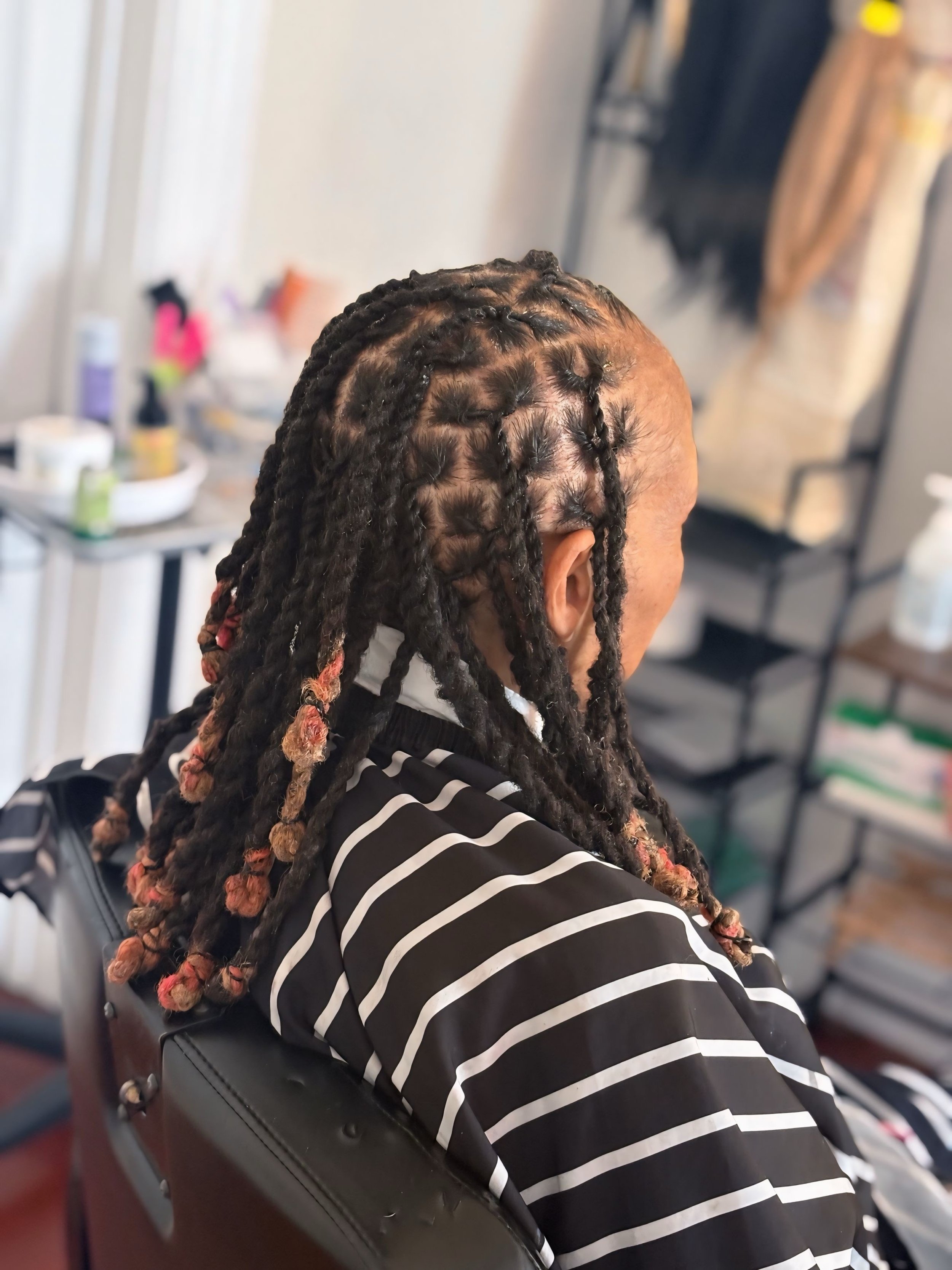 Person with braided hair and colored tips sitting in a salon chair, getting their hair styled.