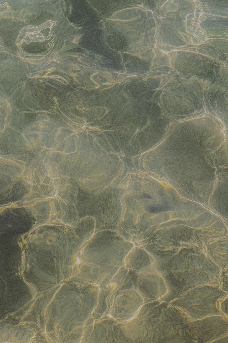 Close-up of water with visible rocks beneath the surface and light reflections creating ripples.