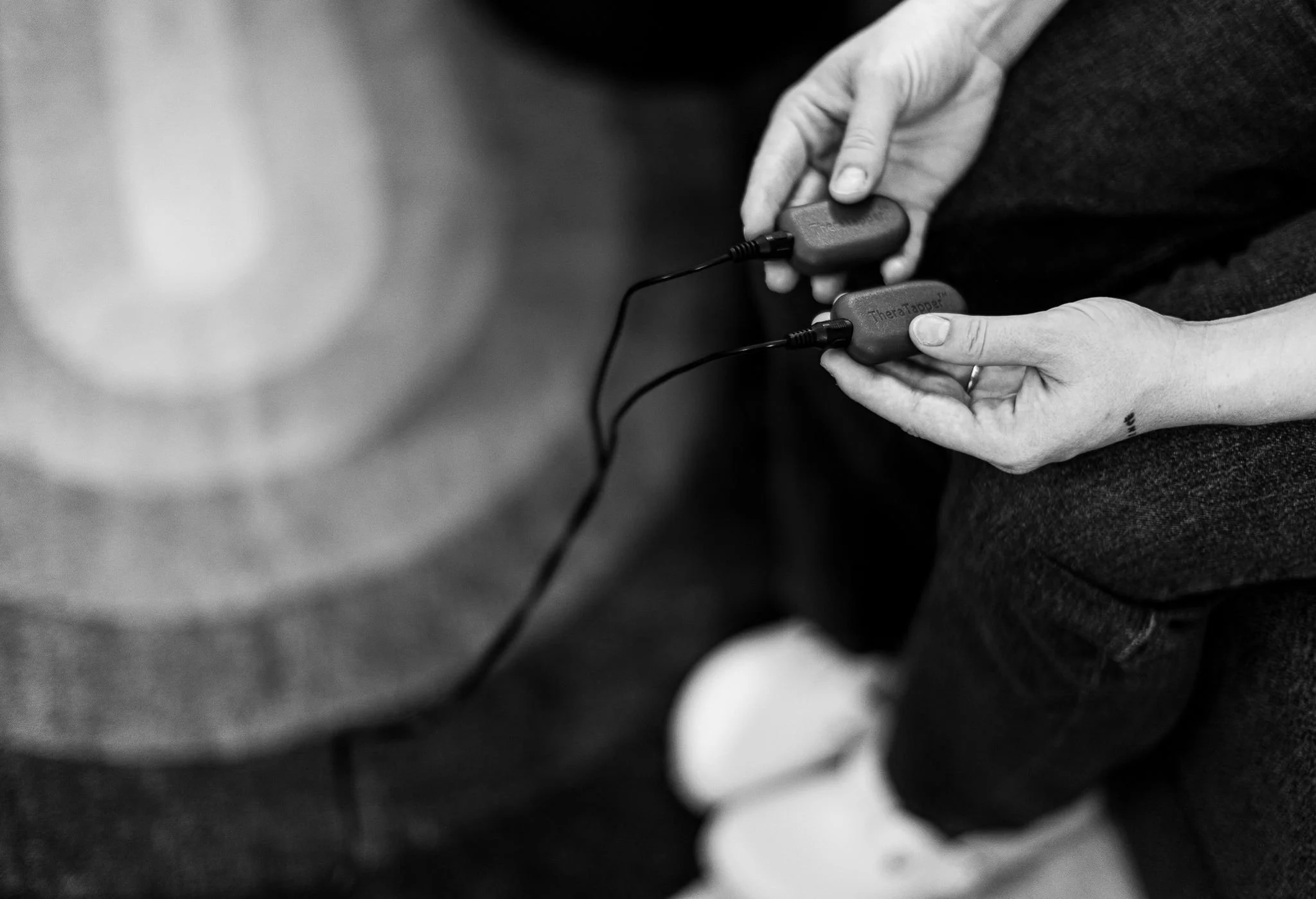 A person holding two small electronic devices connected by a wire, with the words 'TheraTaper' visible on one of them, in black and white.
